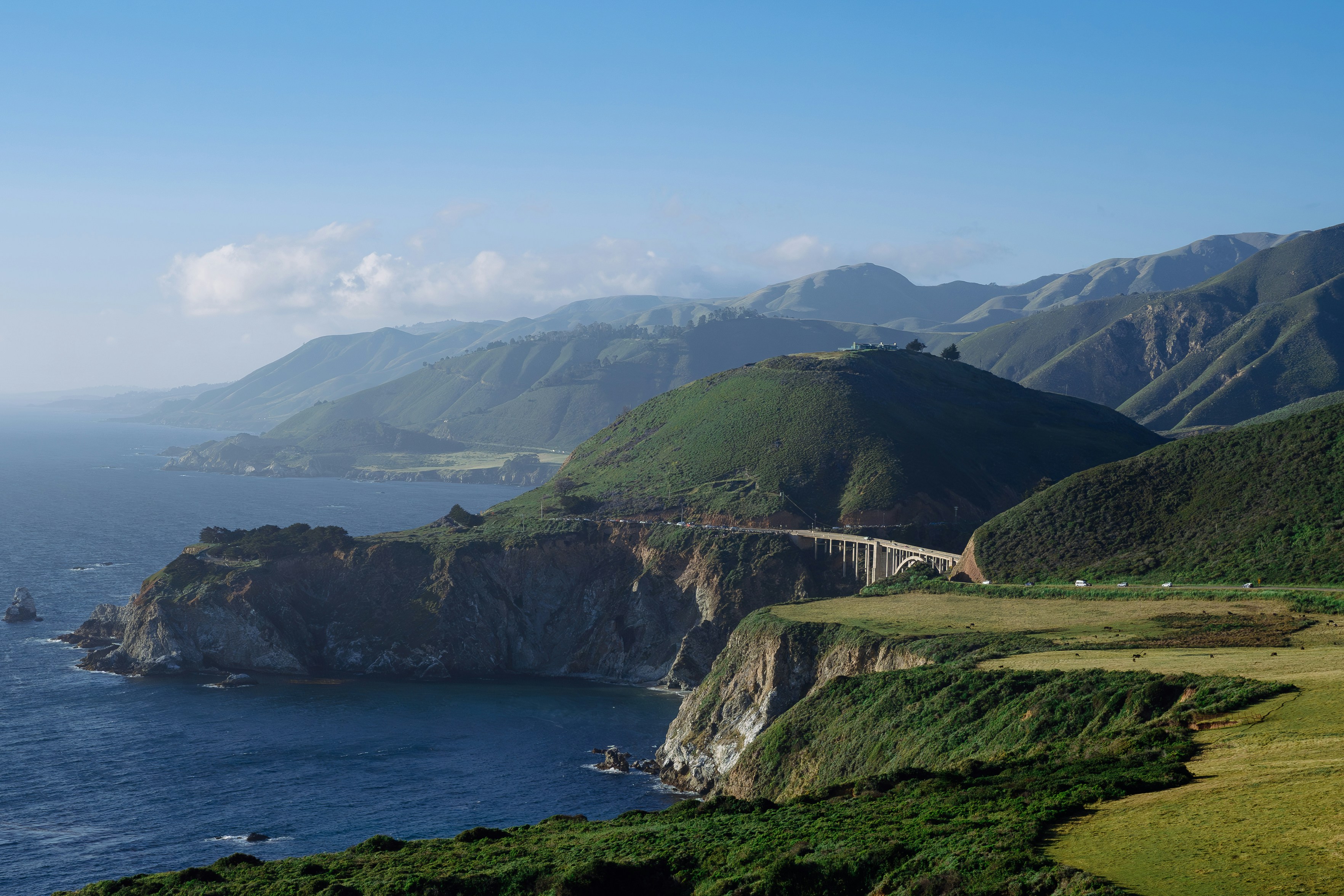 Coastal mountains meet the ocean under a blue sky.