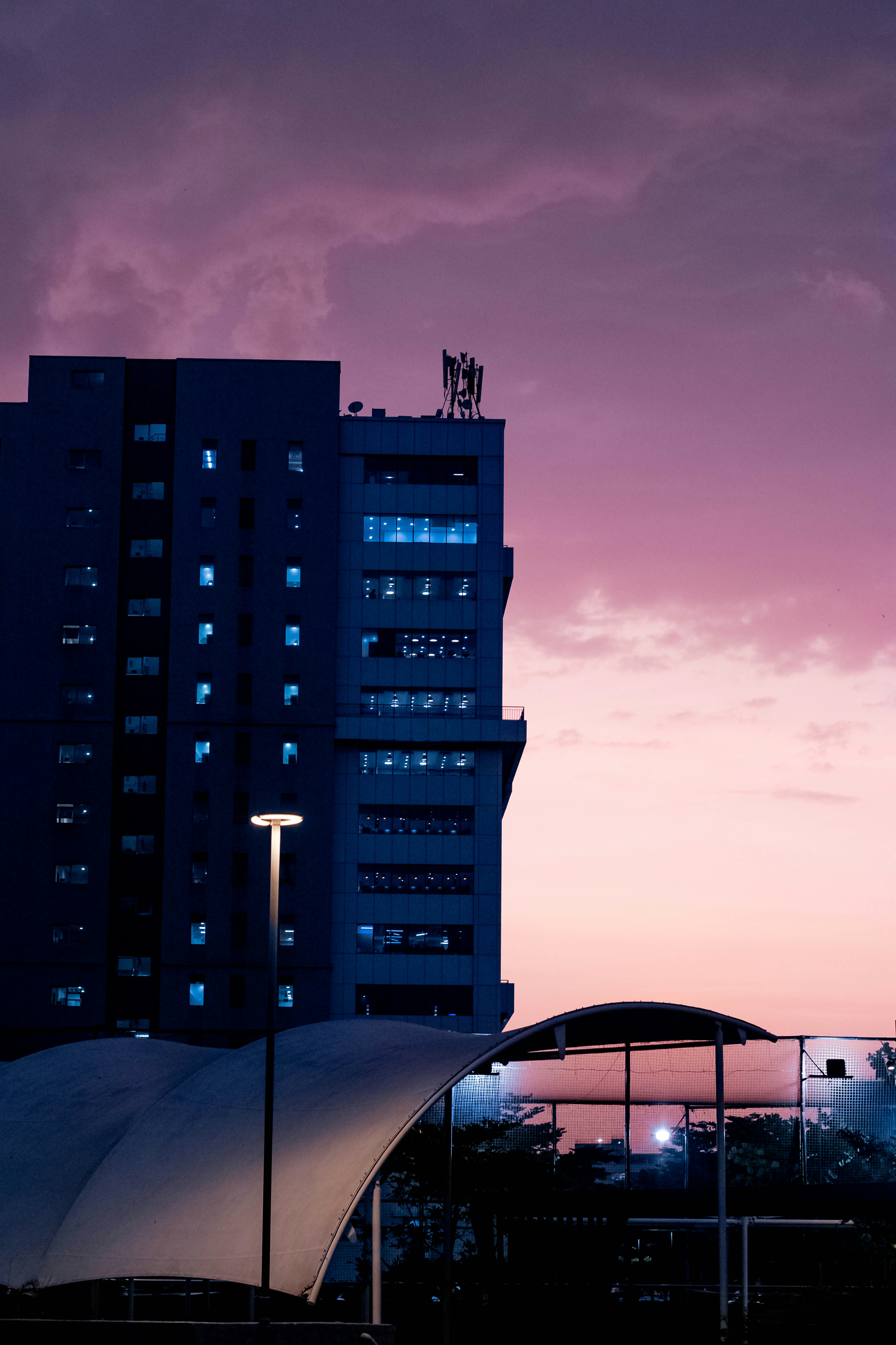 Buildings are illuminated at dusk in a violet sky.
