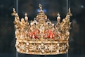 A royal golden crown displayed in a case.