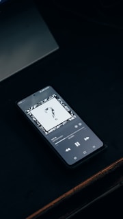 A smartphone plays music on a dark surface.