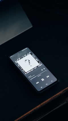 A smartphone plays music on a dark surface.