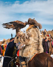 A man is holding a large eagle on horseback.