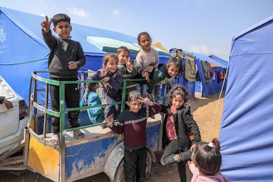 Smiling children pose in front of tents at a refugee camp.