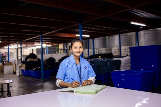 Woman works in a factory, smiling at the camera.