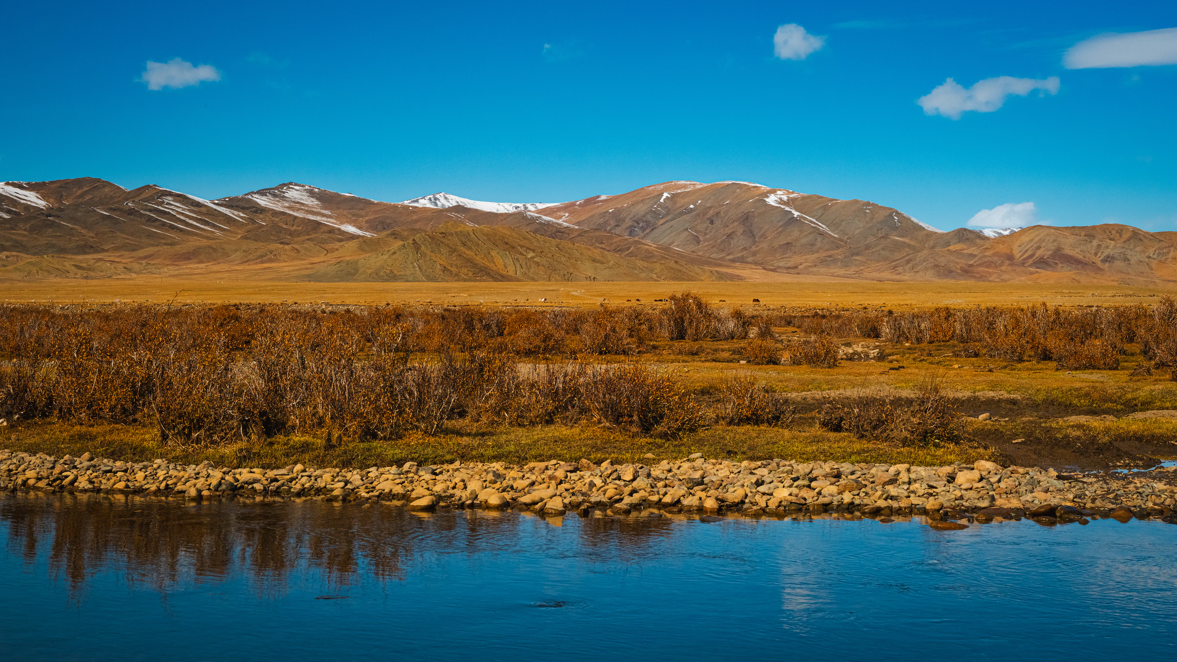 A still river reflecting autumn grass and rust-coloured mountains