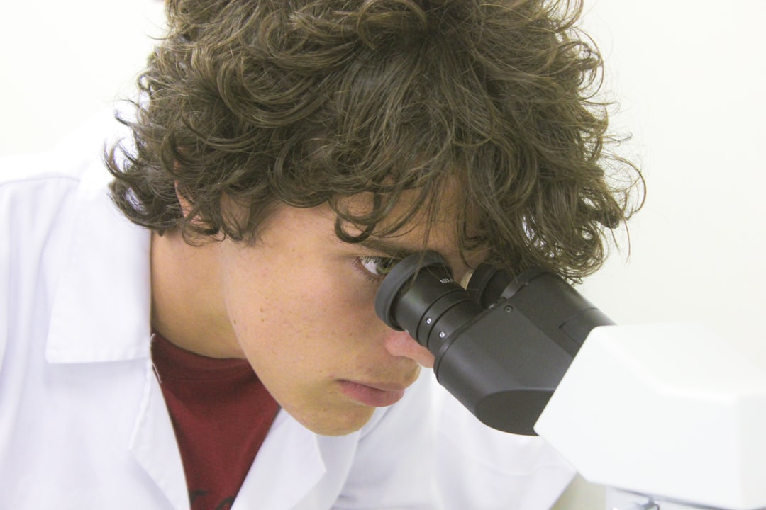 A young scientist examines through a microscope., Man looking into a microscope