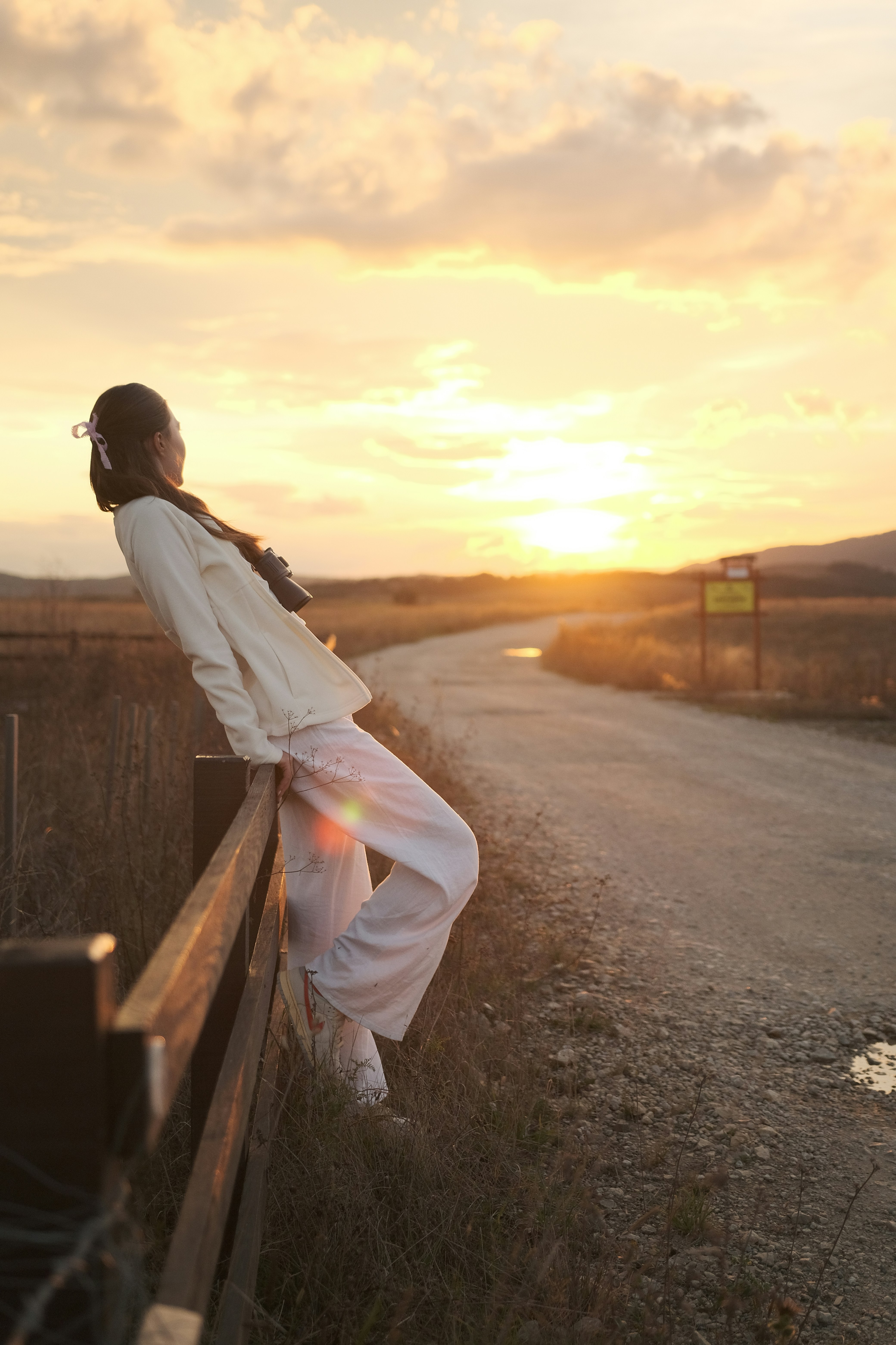 Woman leans on a fence watching the beautiful sunset.