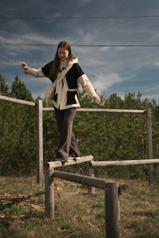 Woman carefully balances on a wooden fence.