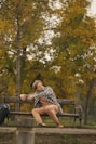 Man relaxes on a park bench surrounded by fall foliage.