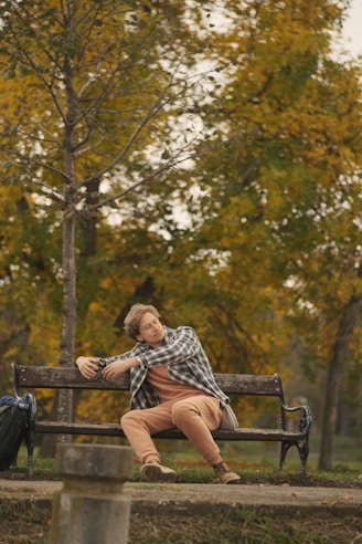 Man relaxes on a park bench surrounded by fall foliage.