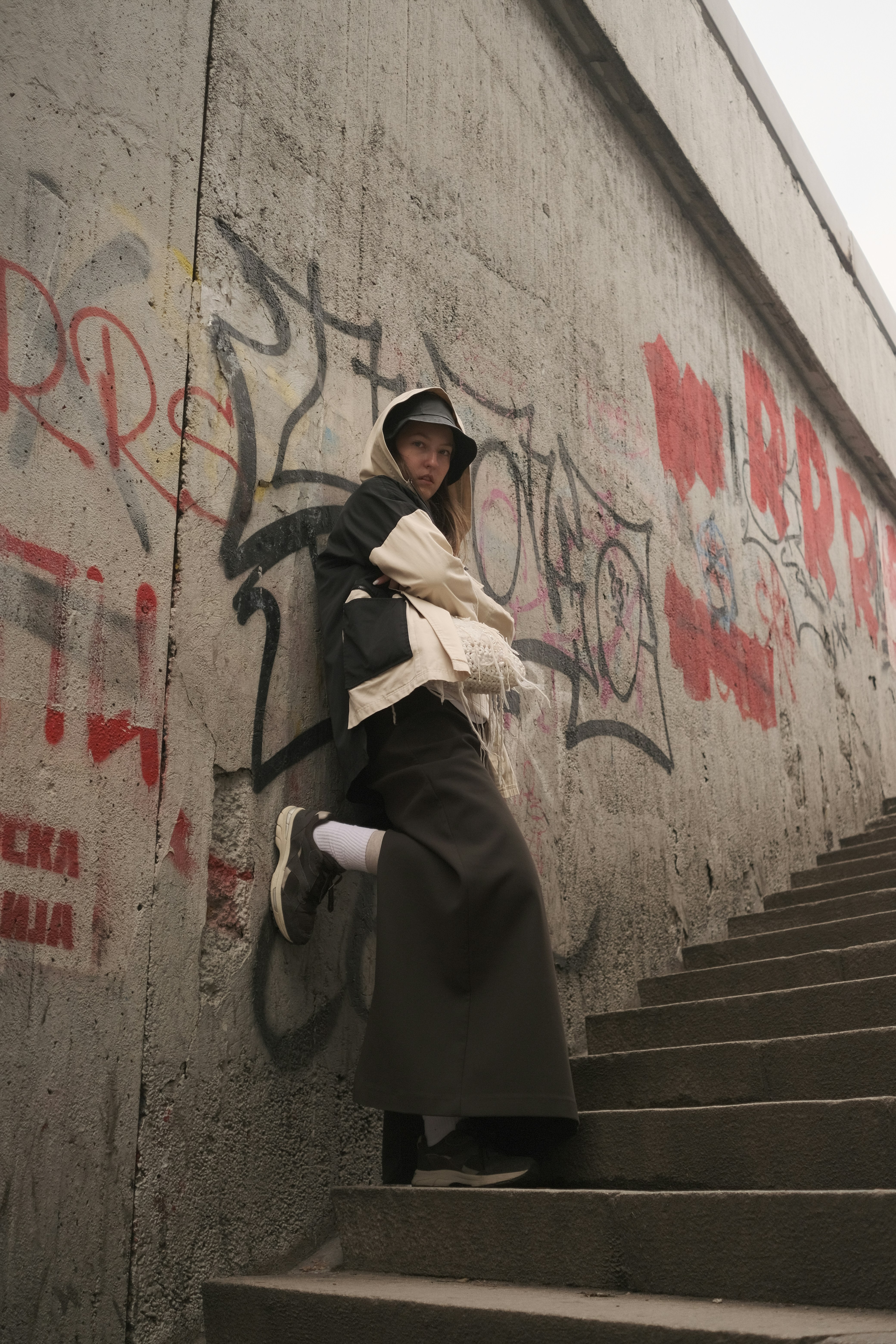 A stylish person poses by a graffiti-covered wall.