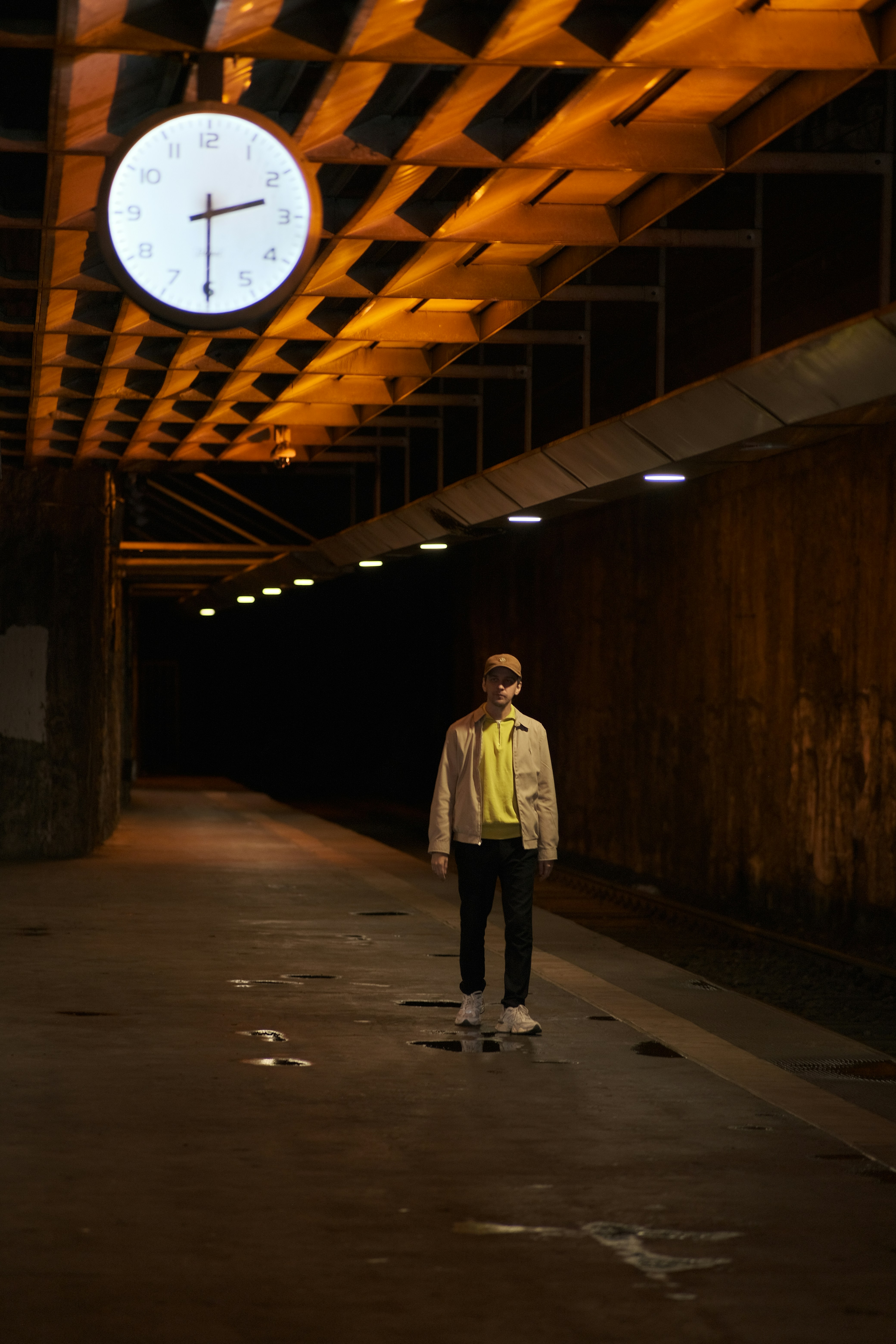 Man stands under a clock in a tunnel.