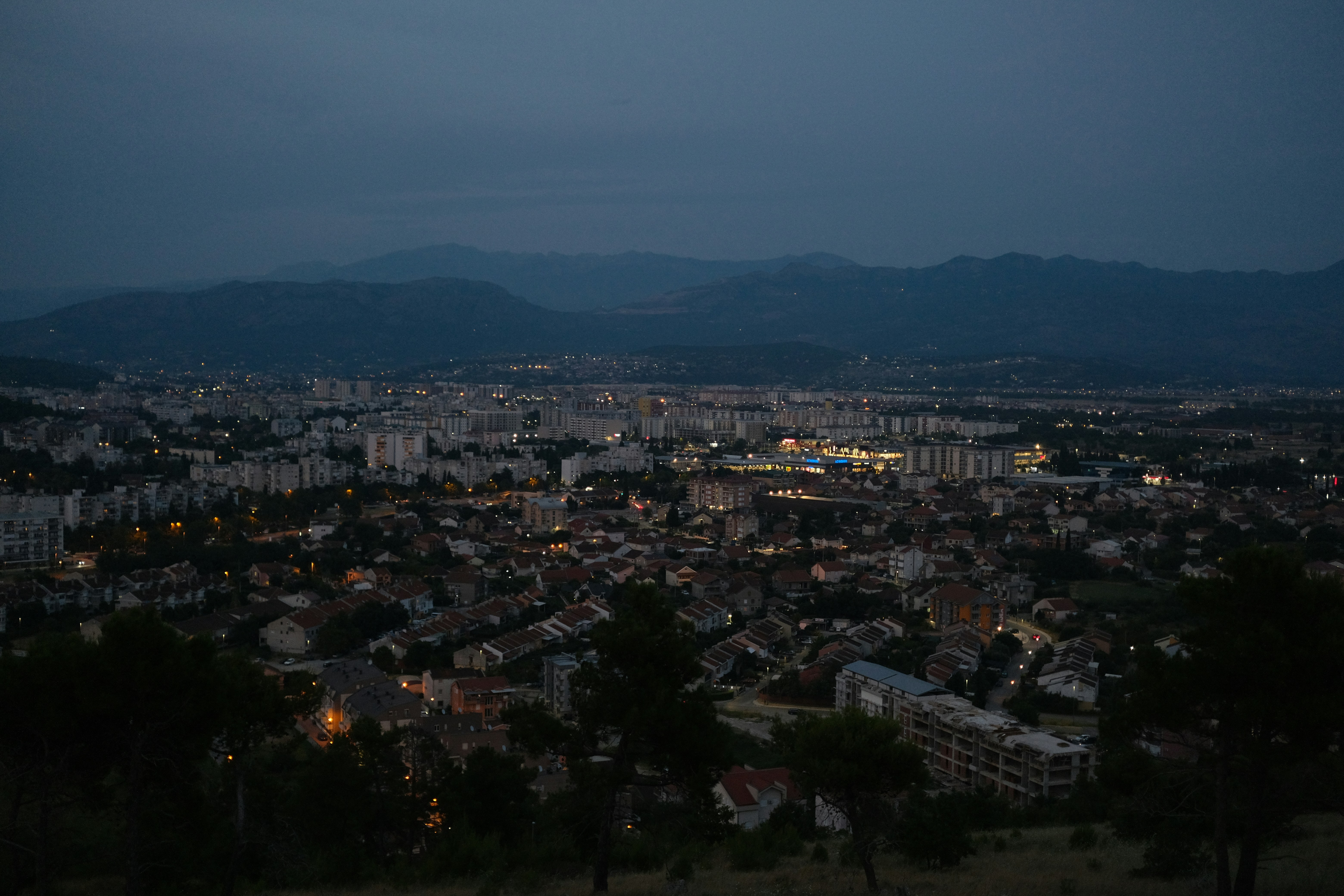 City lights twinkle beneath a dusky mountain backdrop., 