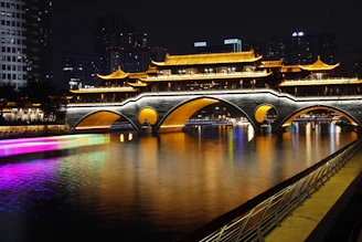 Illuminated bridge at night reflecting in the water.