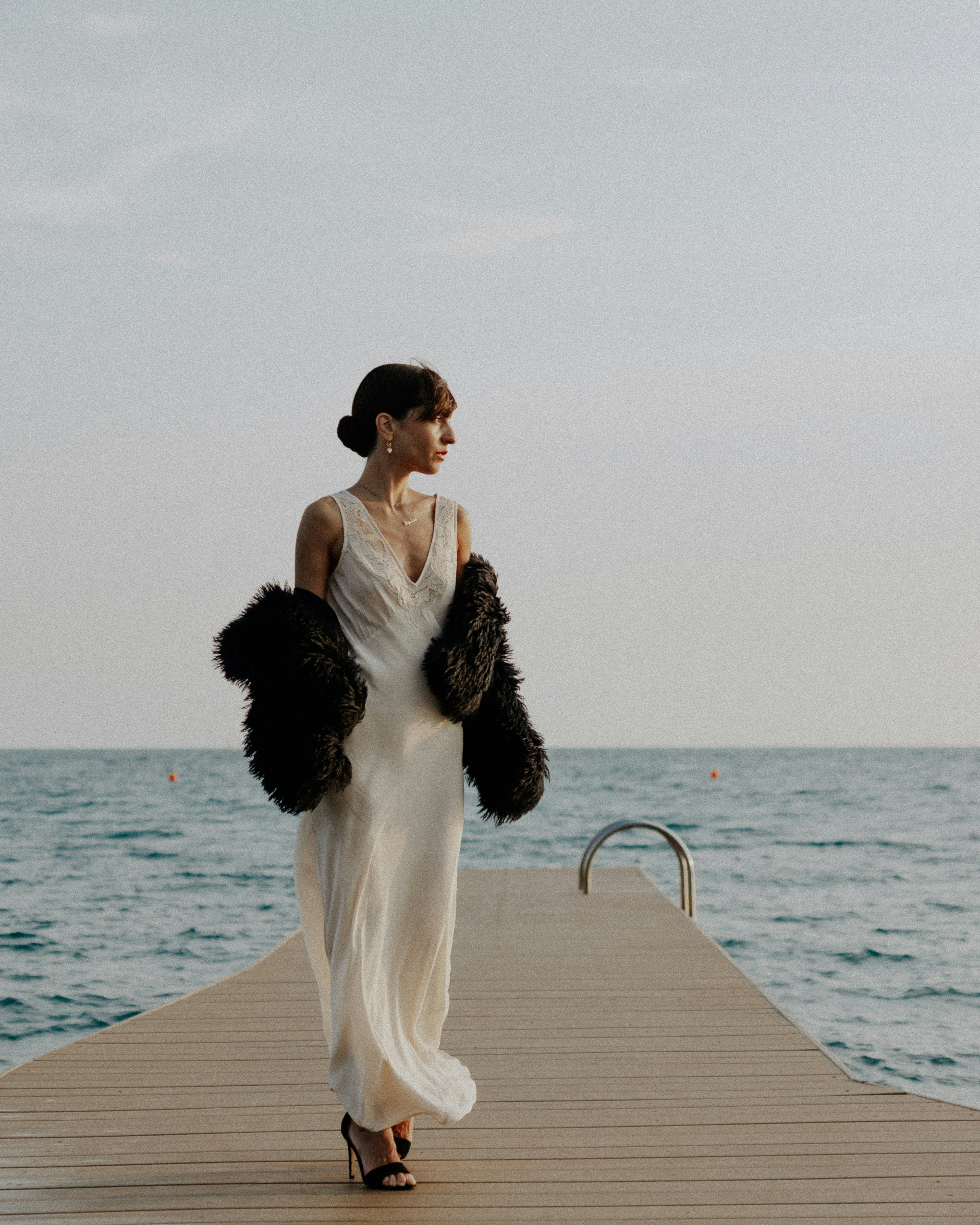 Woman in elegant dress walks on a pier.