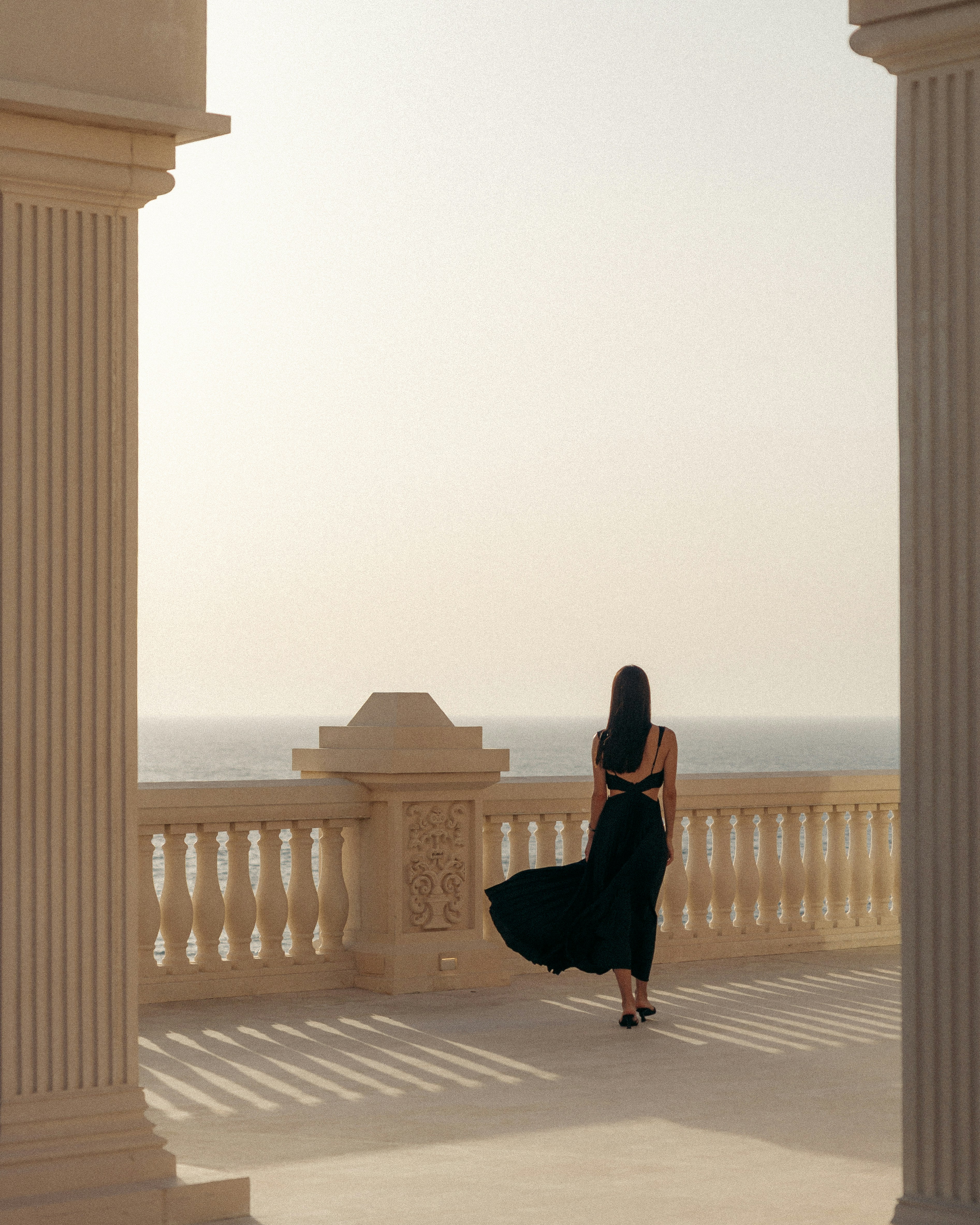 Woman in a black dress walks toward the sea.