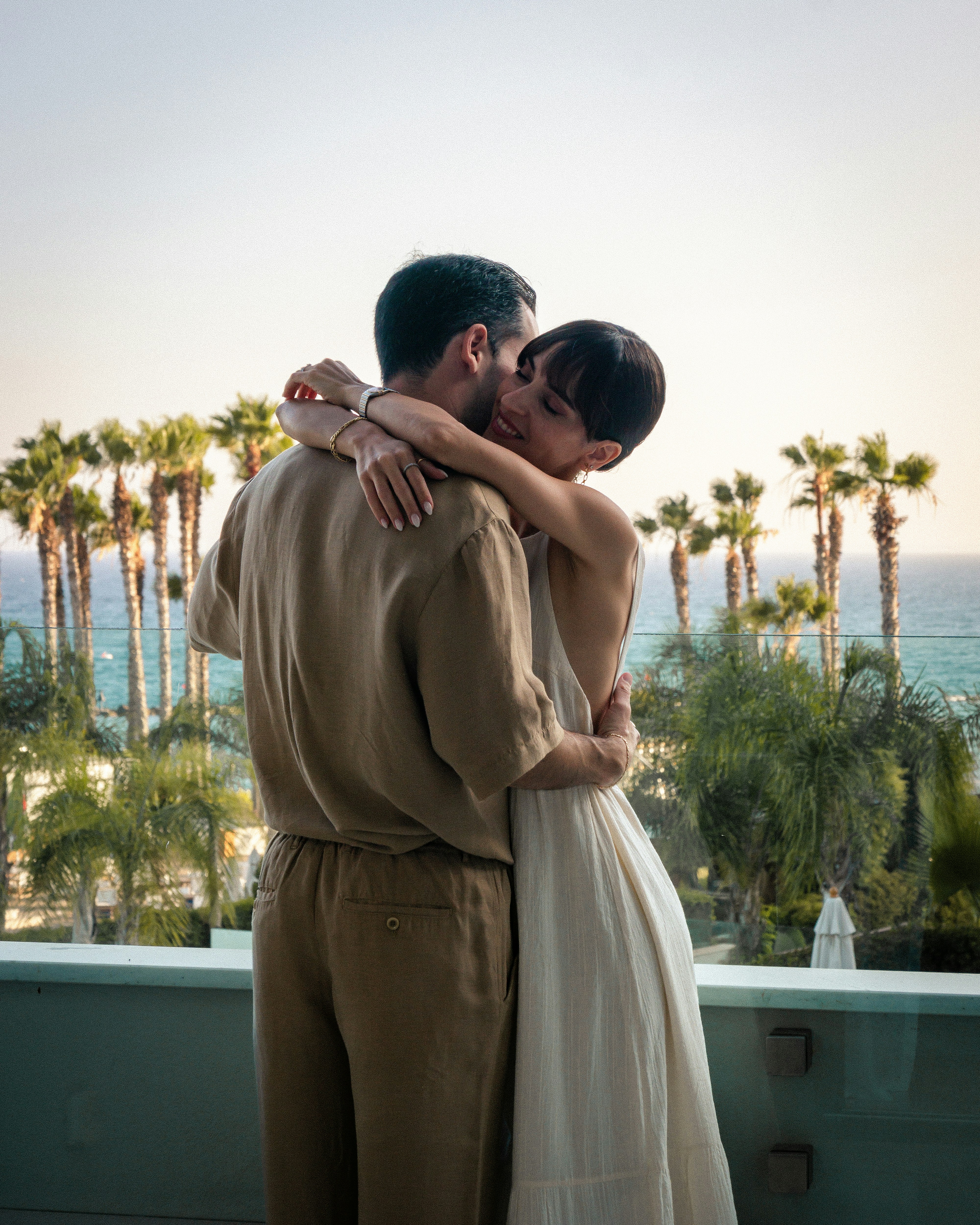 Couple embraces on a balcony overlooking the ocean.