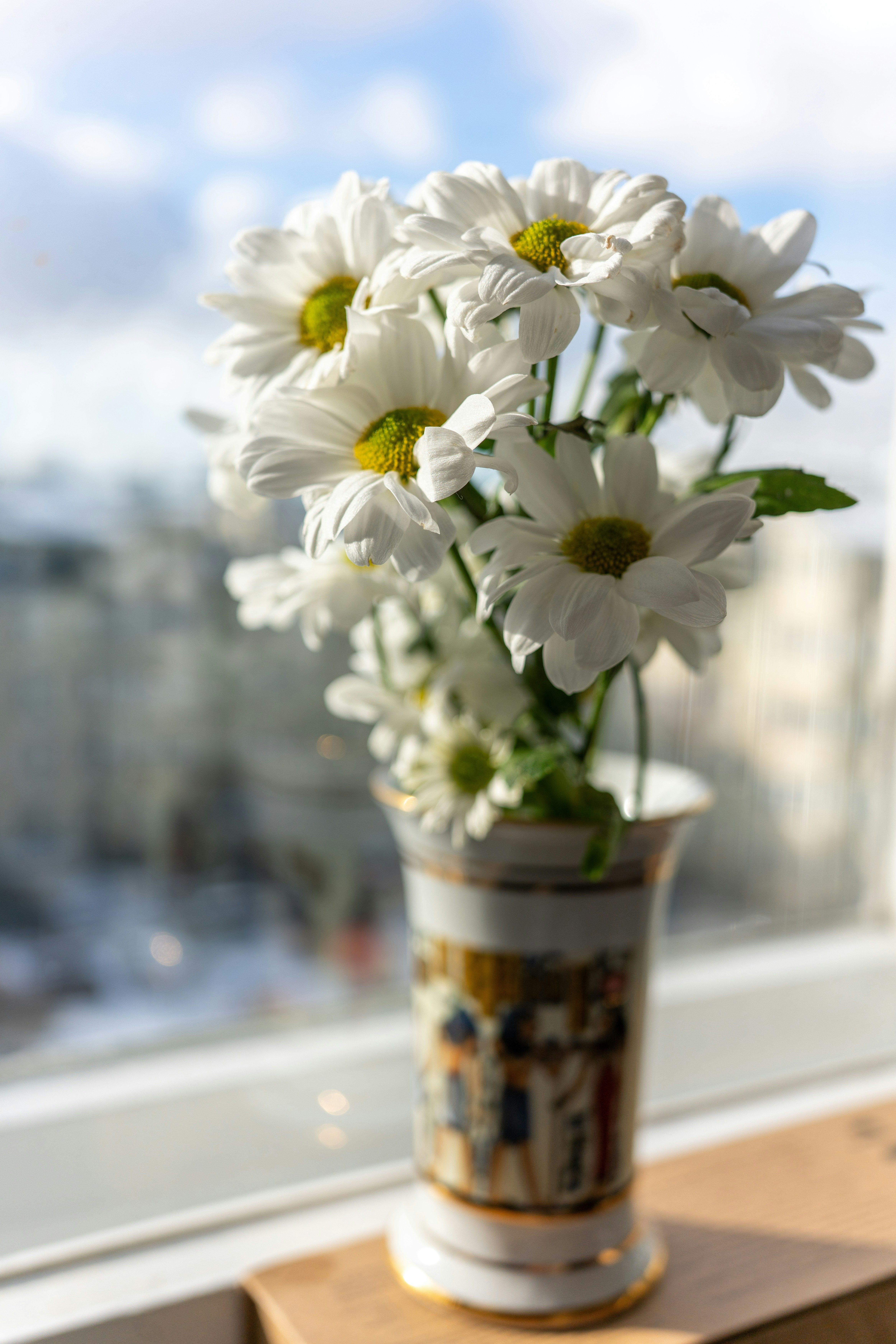 Weiße Gänseblümchen stehen in einer Vase am Fenster.