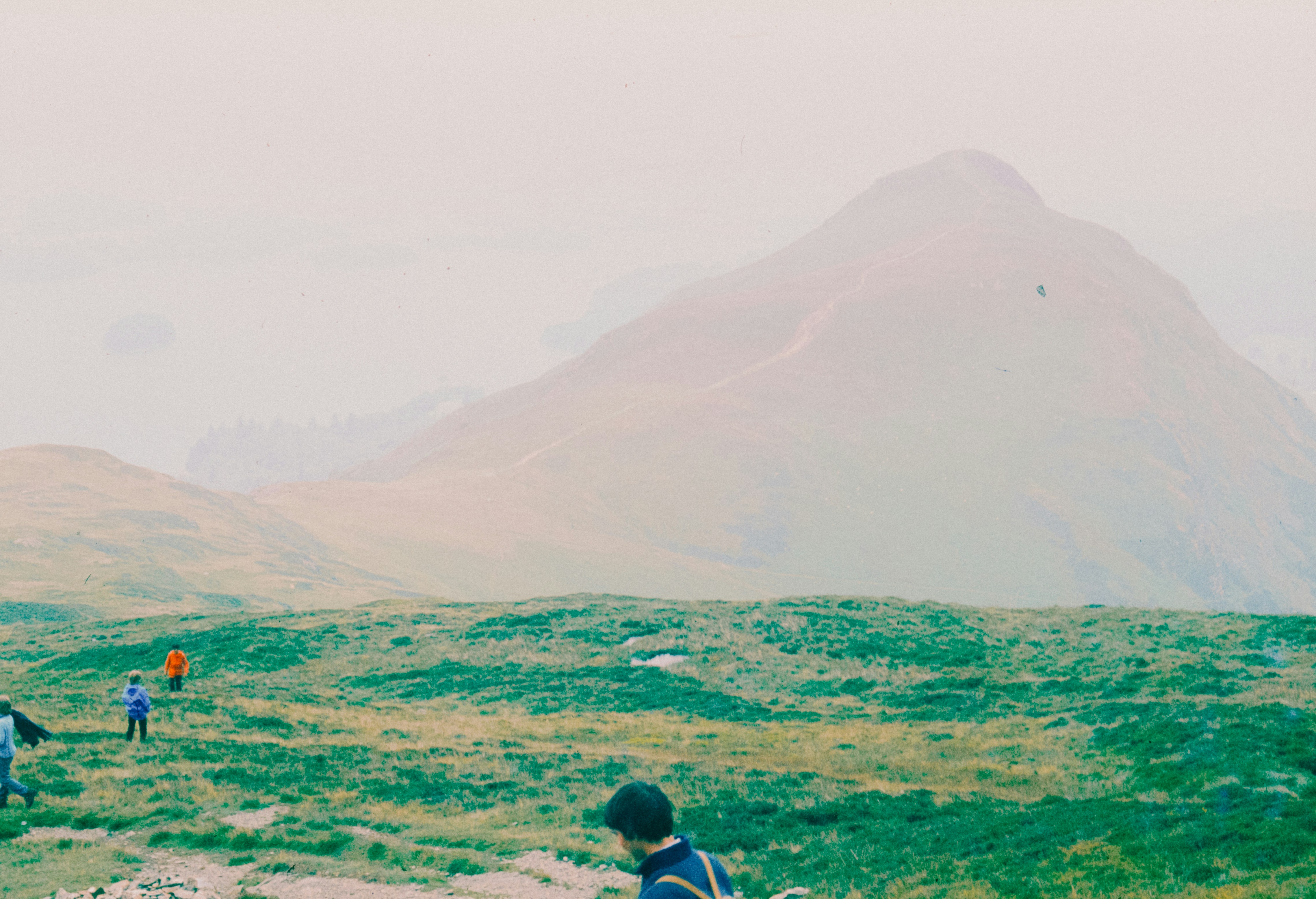 People hike toward a mountain on a green field.