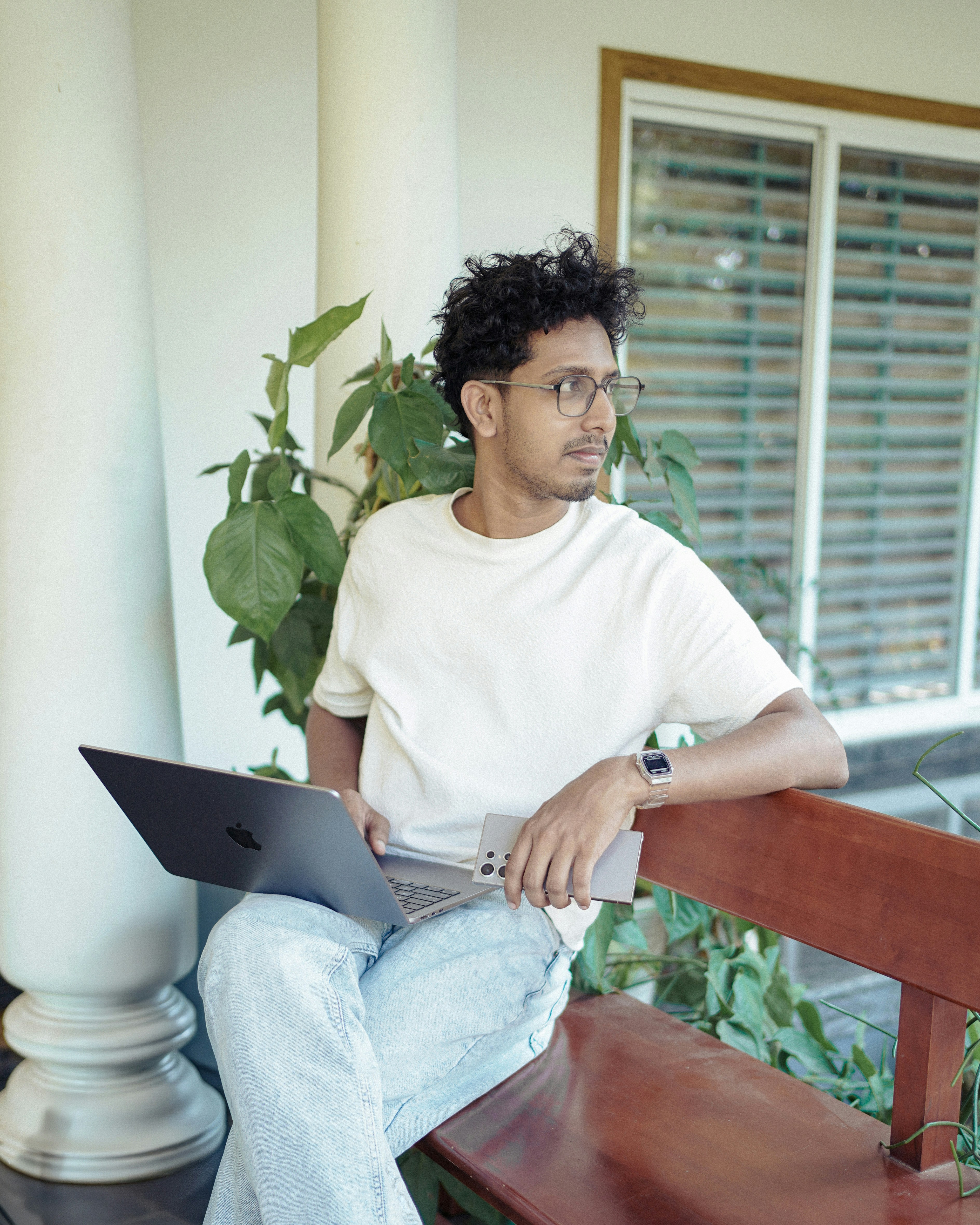 Man with laptop and phone gazes thoughtfully.