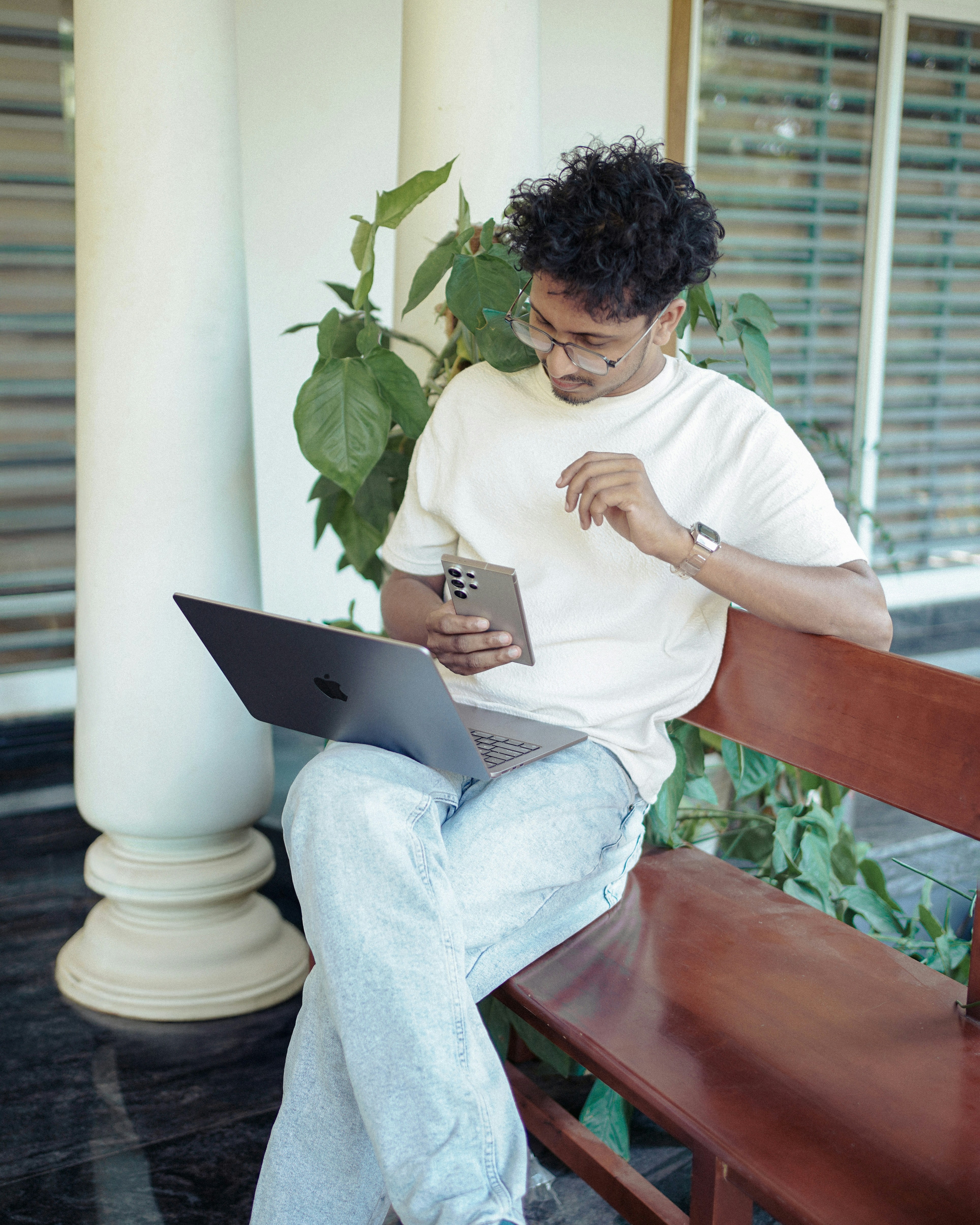 Man is using phone and laptop outdoors.