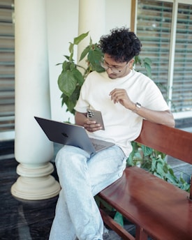 Man is using phone and laptop outdoors.