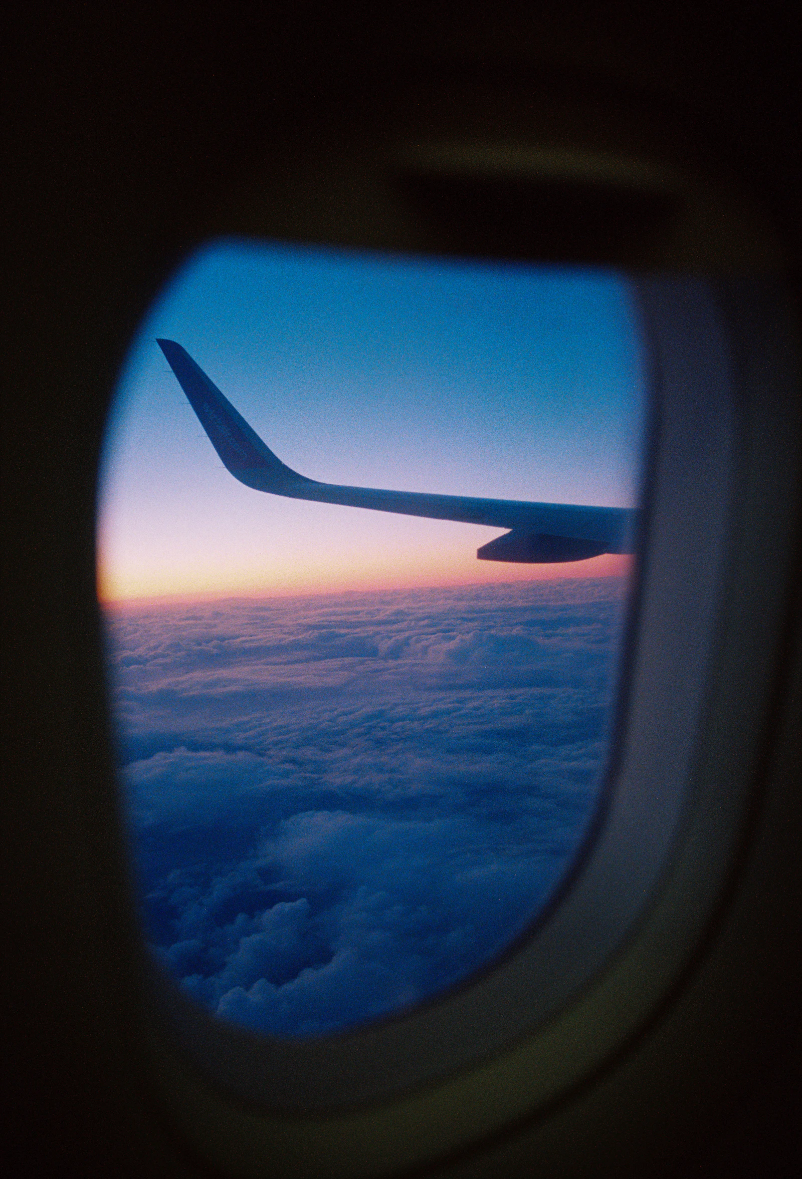 Aircraft wing seen through a cabin window above a sea of clouds at sunset