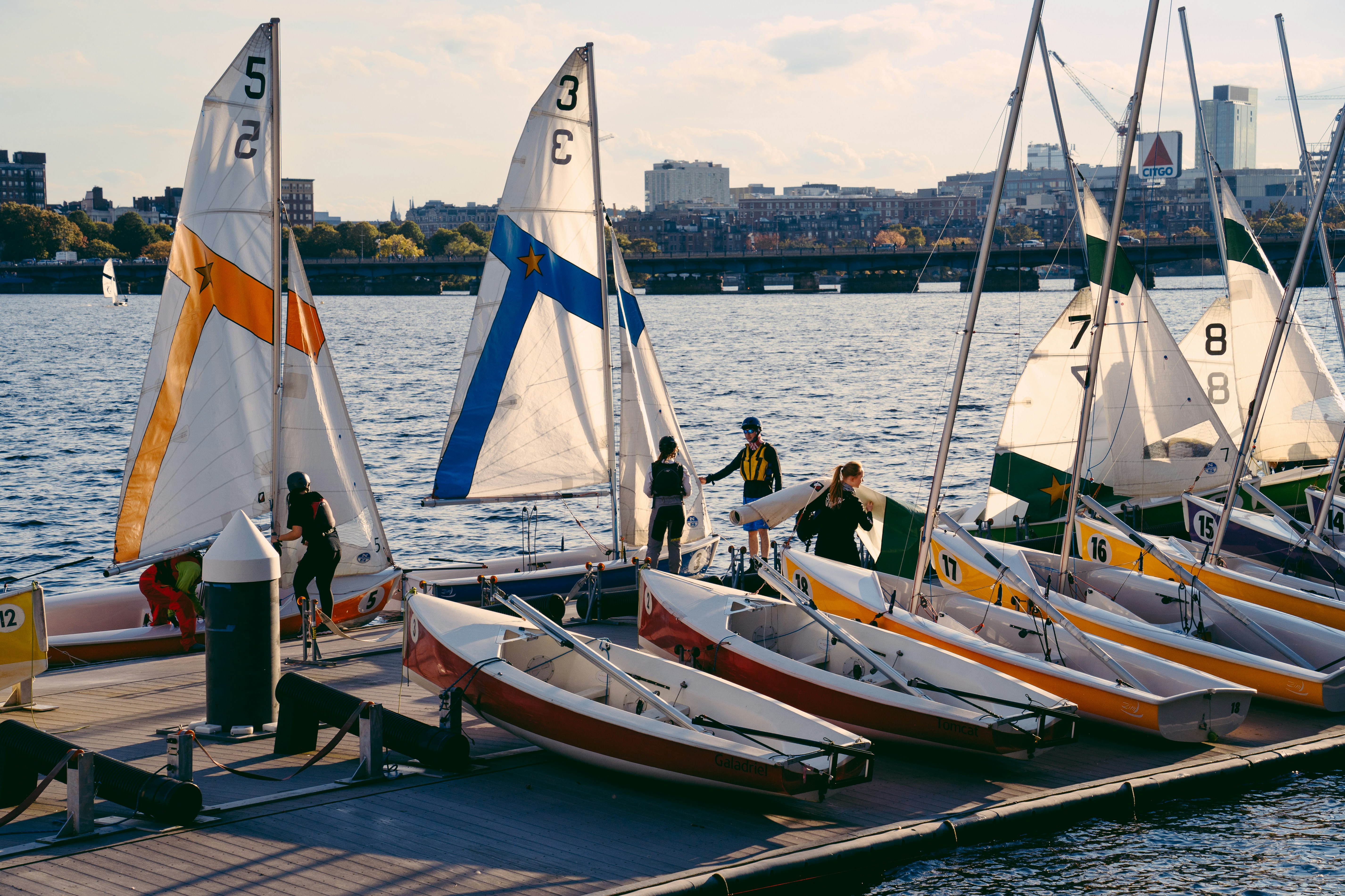 Sailboats line a dock with people preparing to sail.