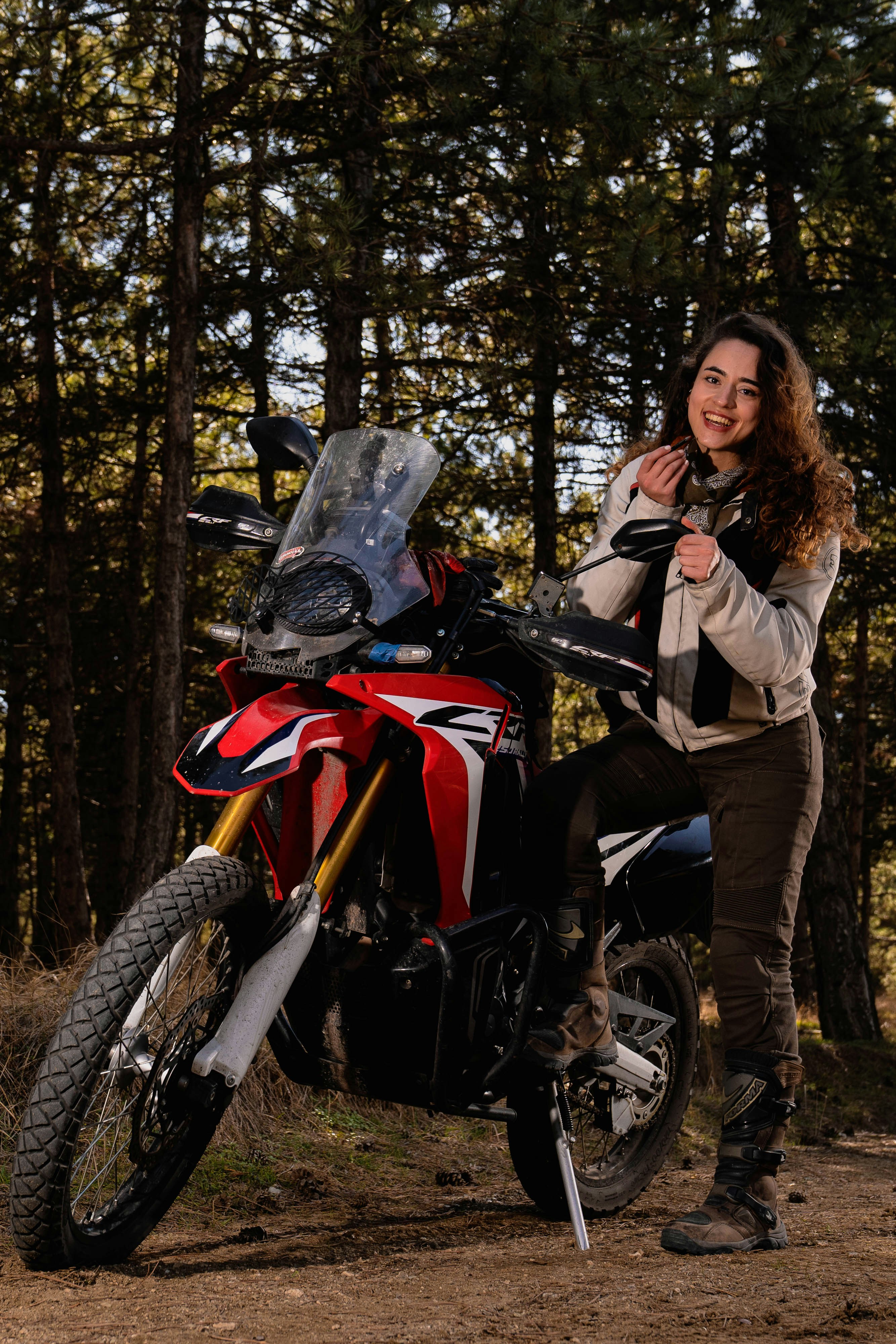Woman smiles next to a motorcycle in the woods.