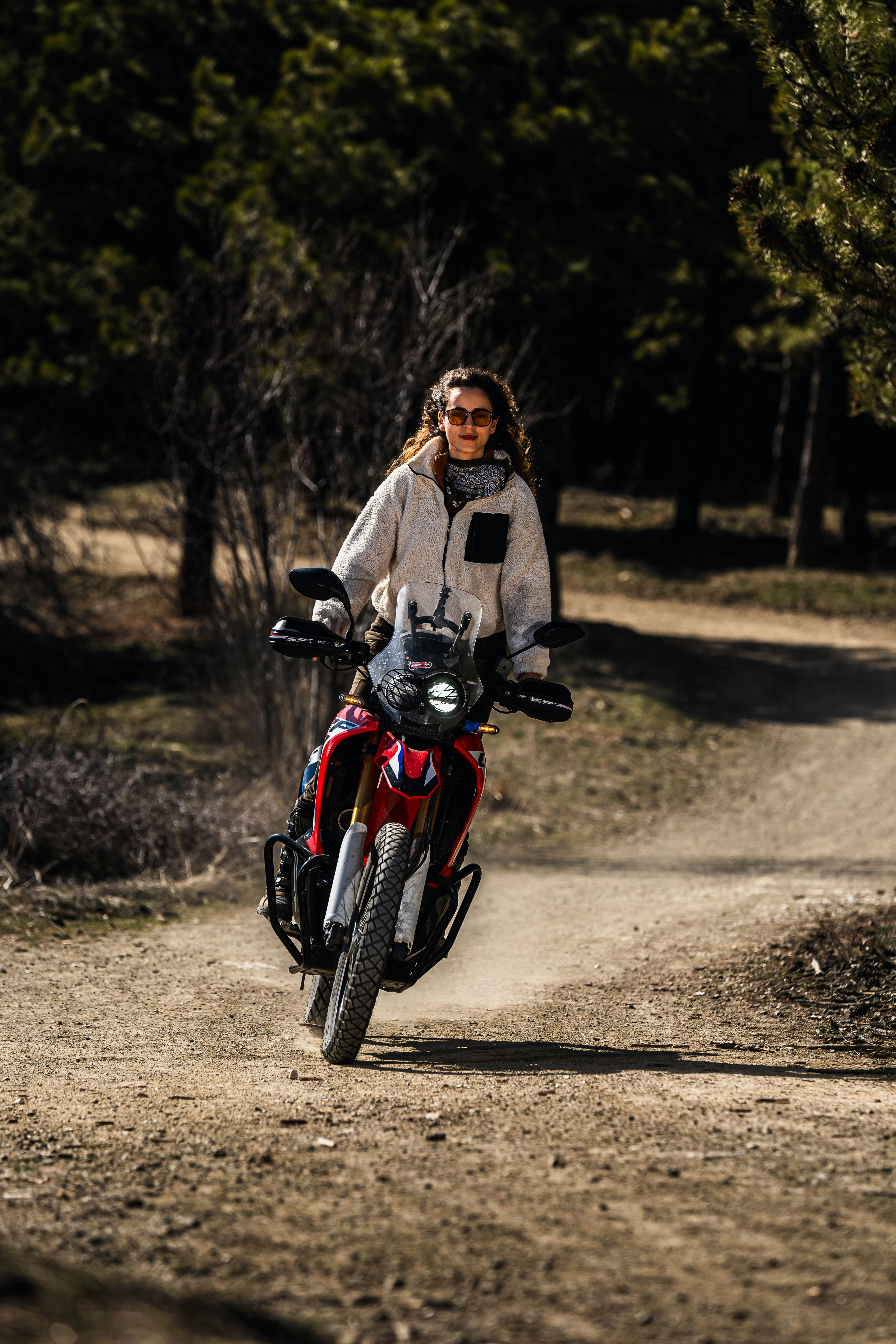Woman rides motorcycle on a dirt road.
