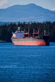 A cargo ship sails near mountains.