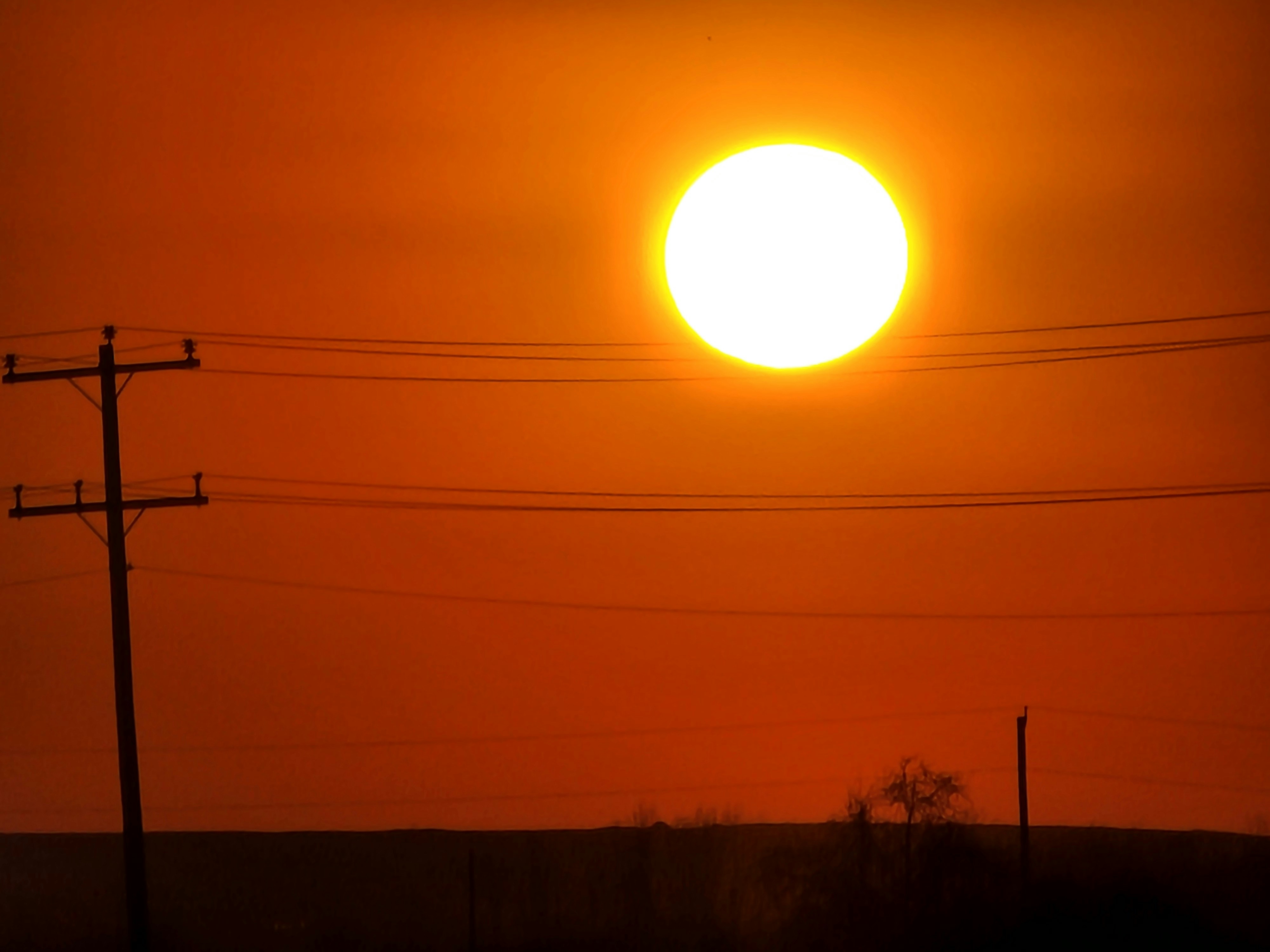 The sun sets over a landscape with power lines.