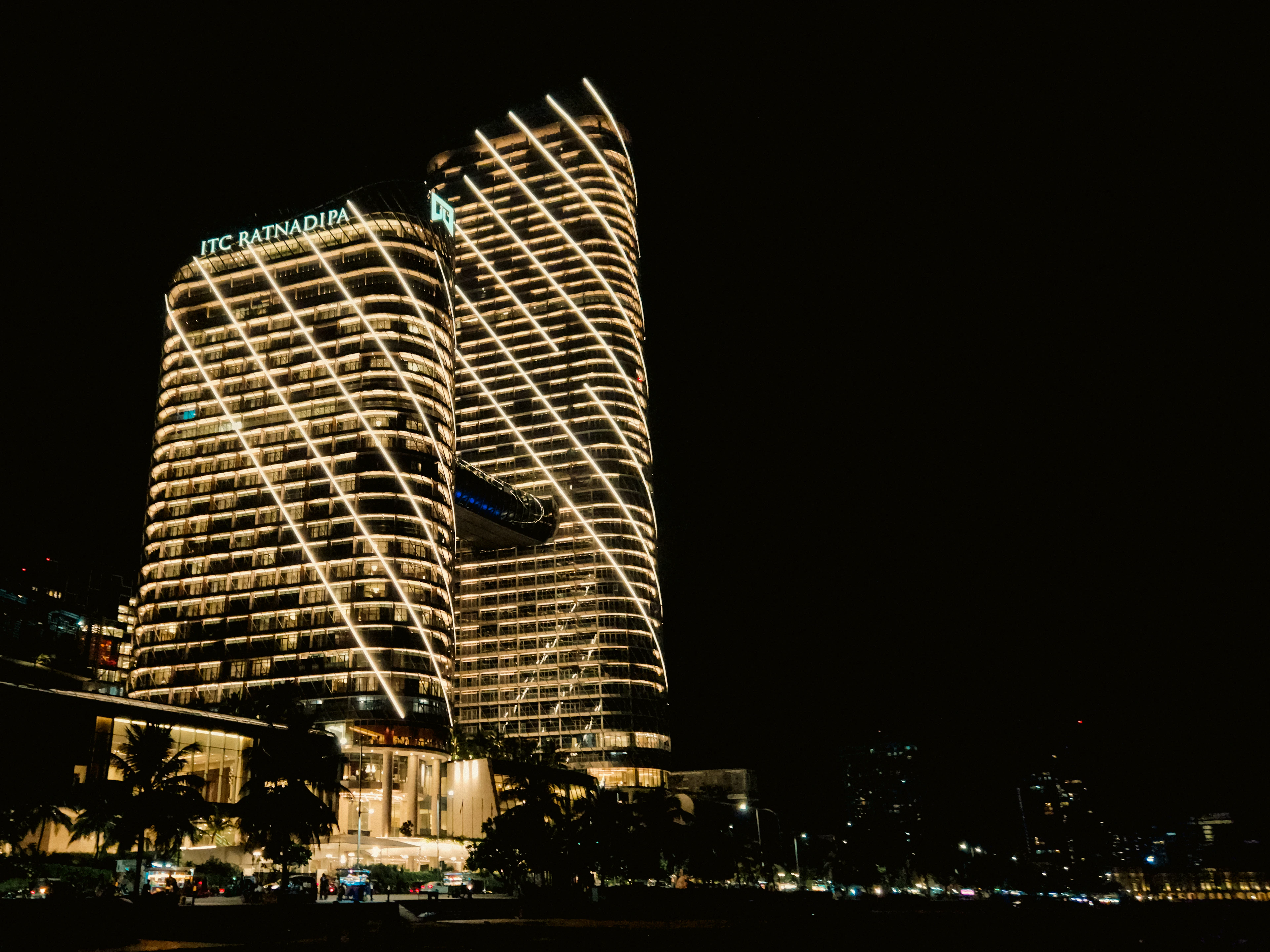 A wave-patterned skyscraper glows gold against Colombo's night skyline, with city lights spread below.