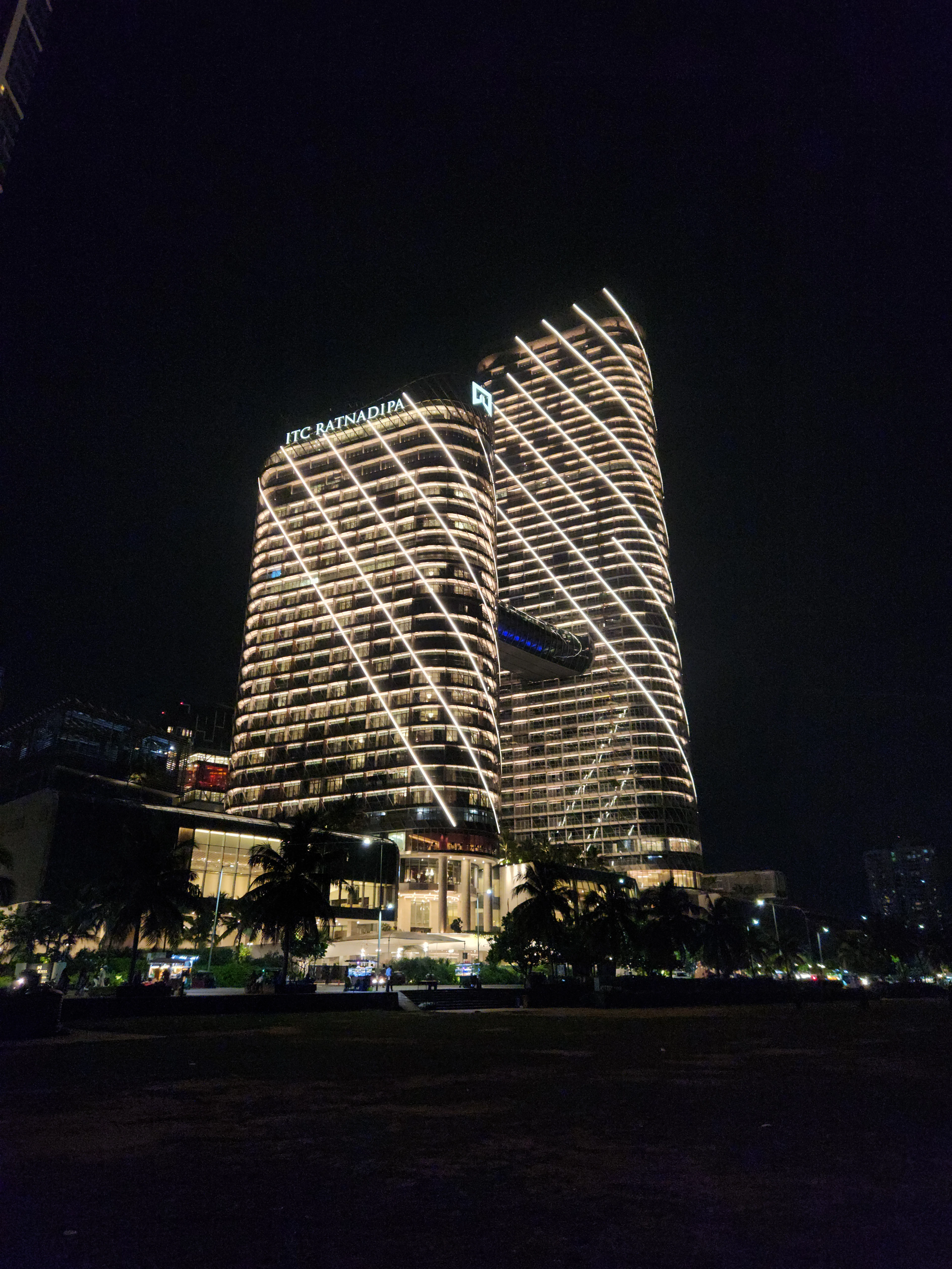 A brightly lit modern high-rise hotel tower glowing at night above the open lawn of Galle Face Green.