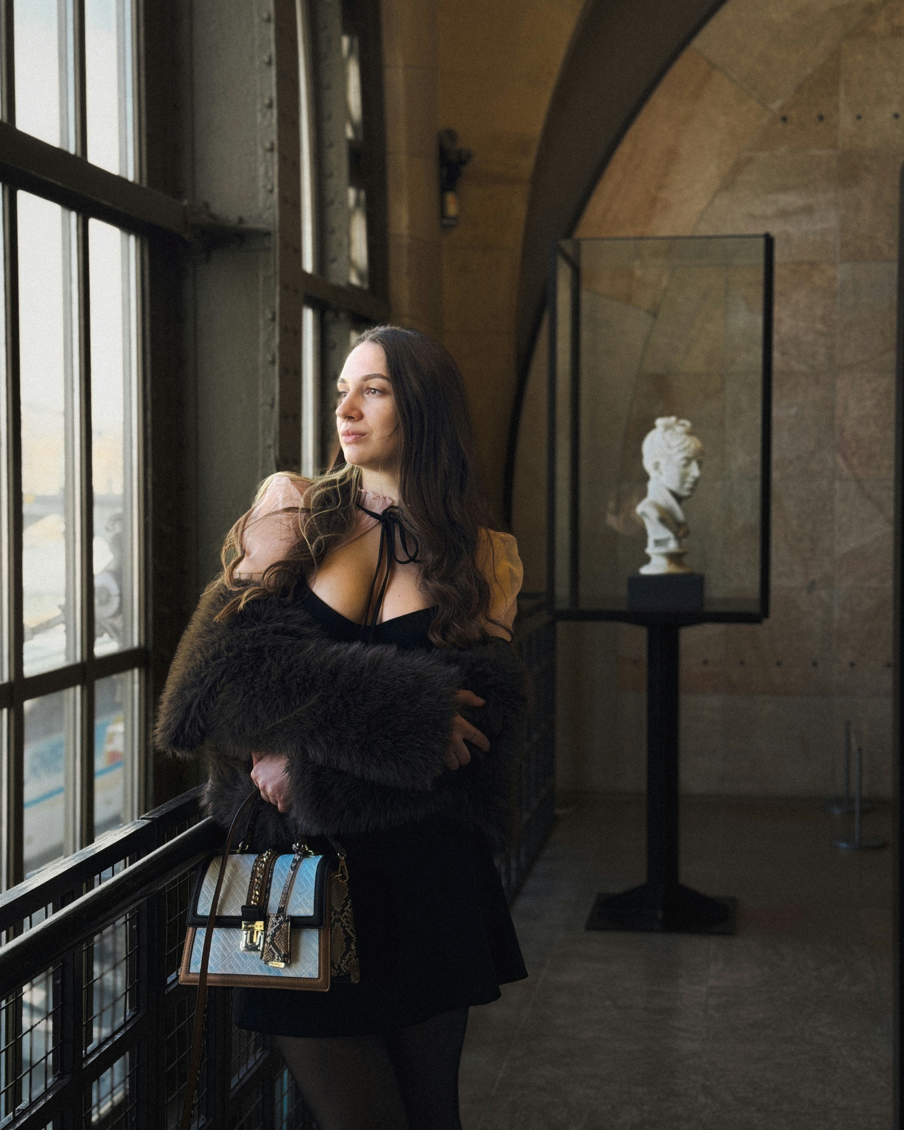 Woman poses elegantly near a museum window.