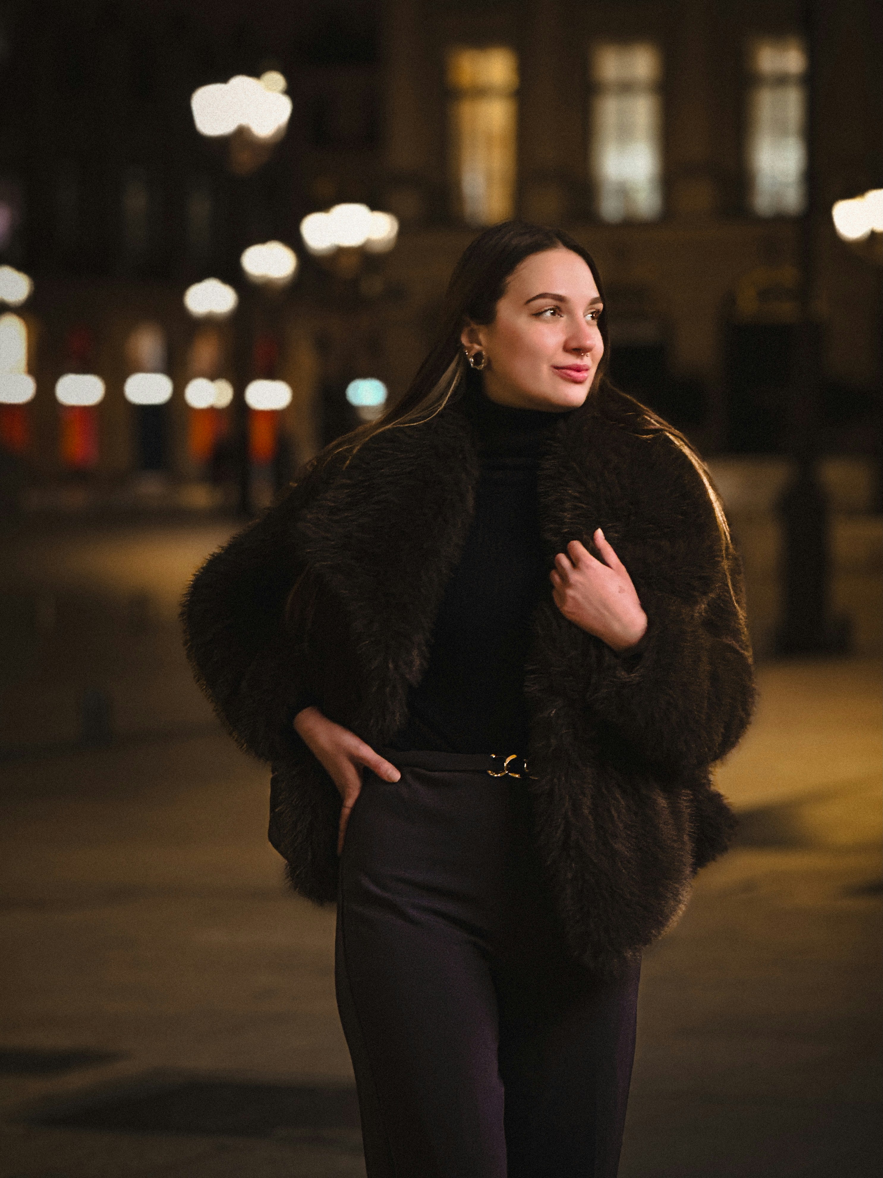 Woman in a fur coat poses at night.