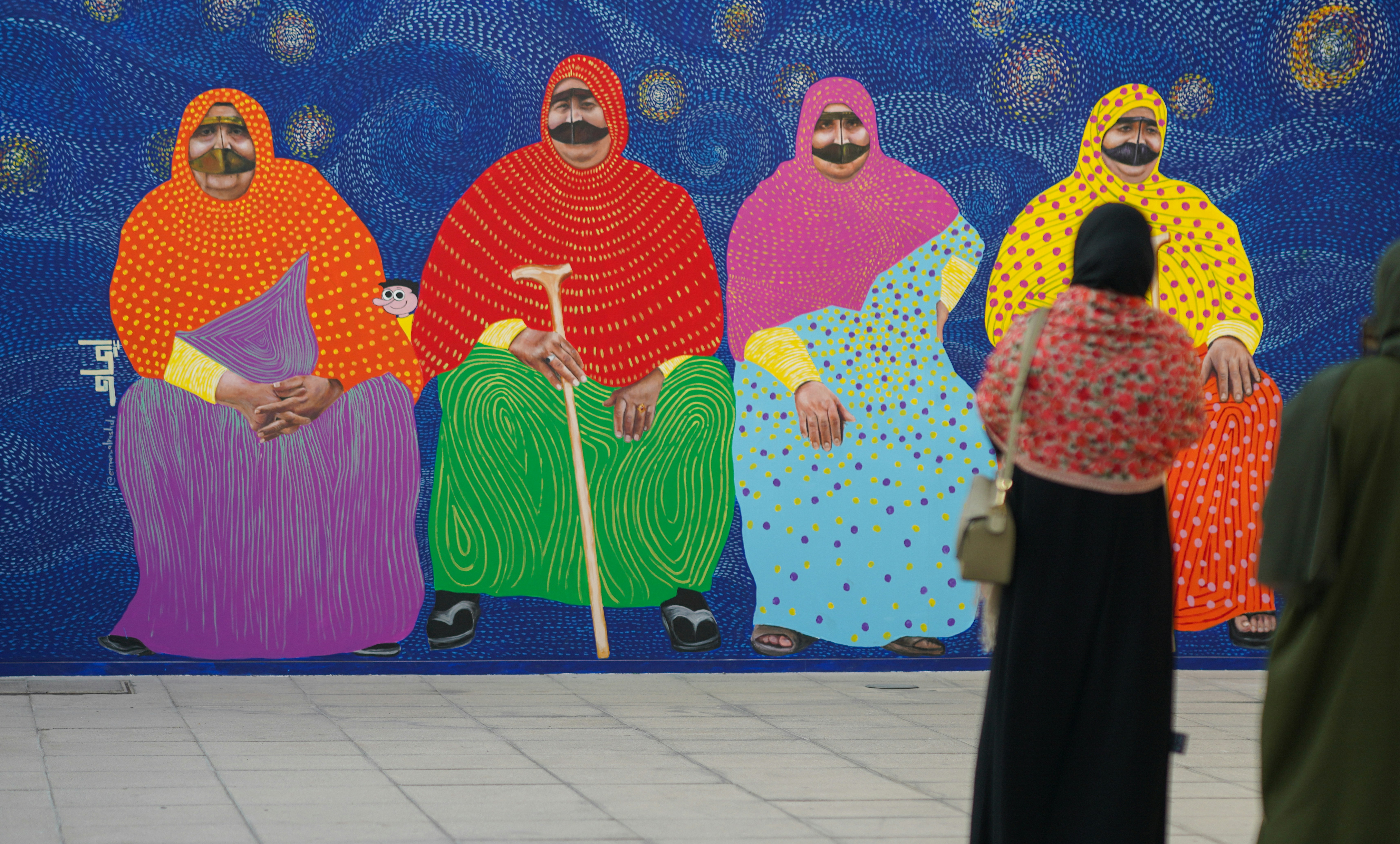 People admire a colorful mural of seated figures.