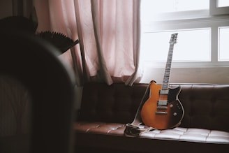 A guitar leans against a couch by a window.
