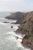 Rugged coastline meets crashing waves under a cloudy sky.