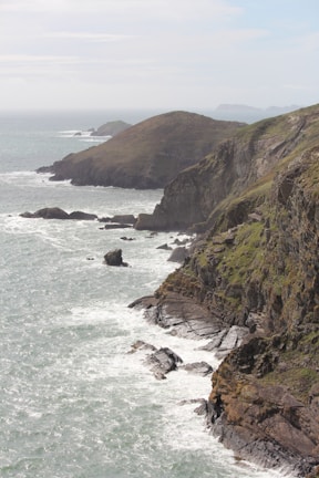 Rugged coastline meets crashing waves under a cloudy sky.