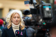 A female reporter is standing in front of a camera.