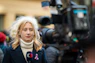 A female reporter is standing in front of a camera.