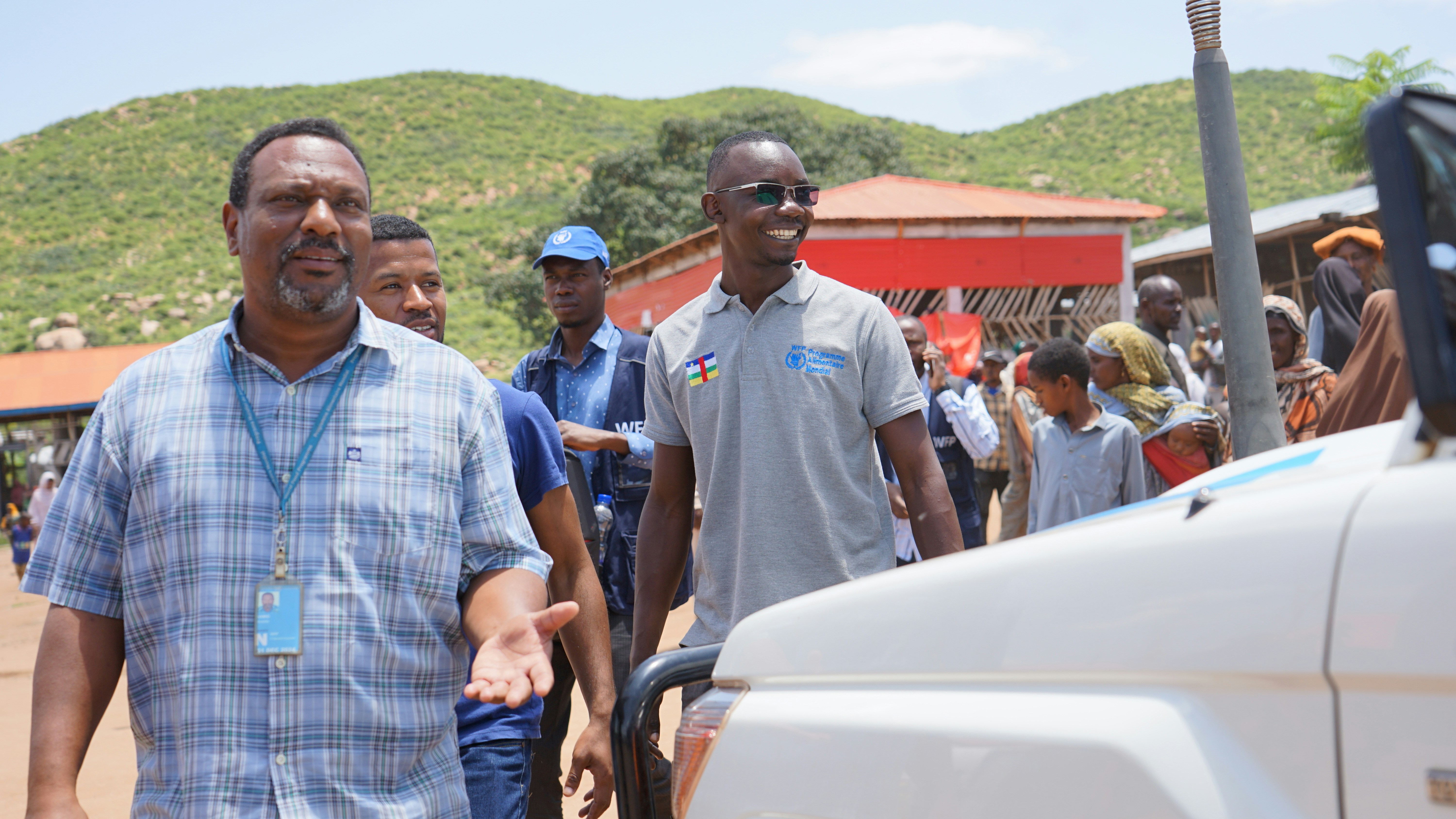 A group of people walk down a sunny street.