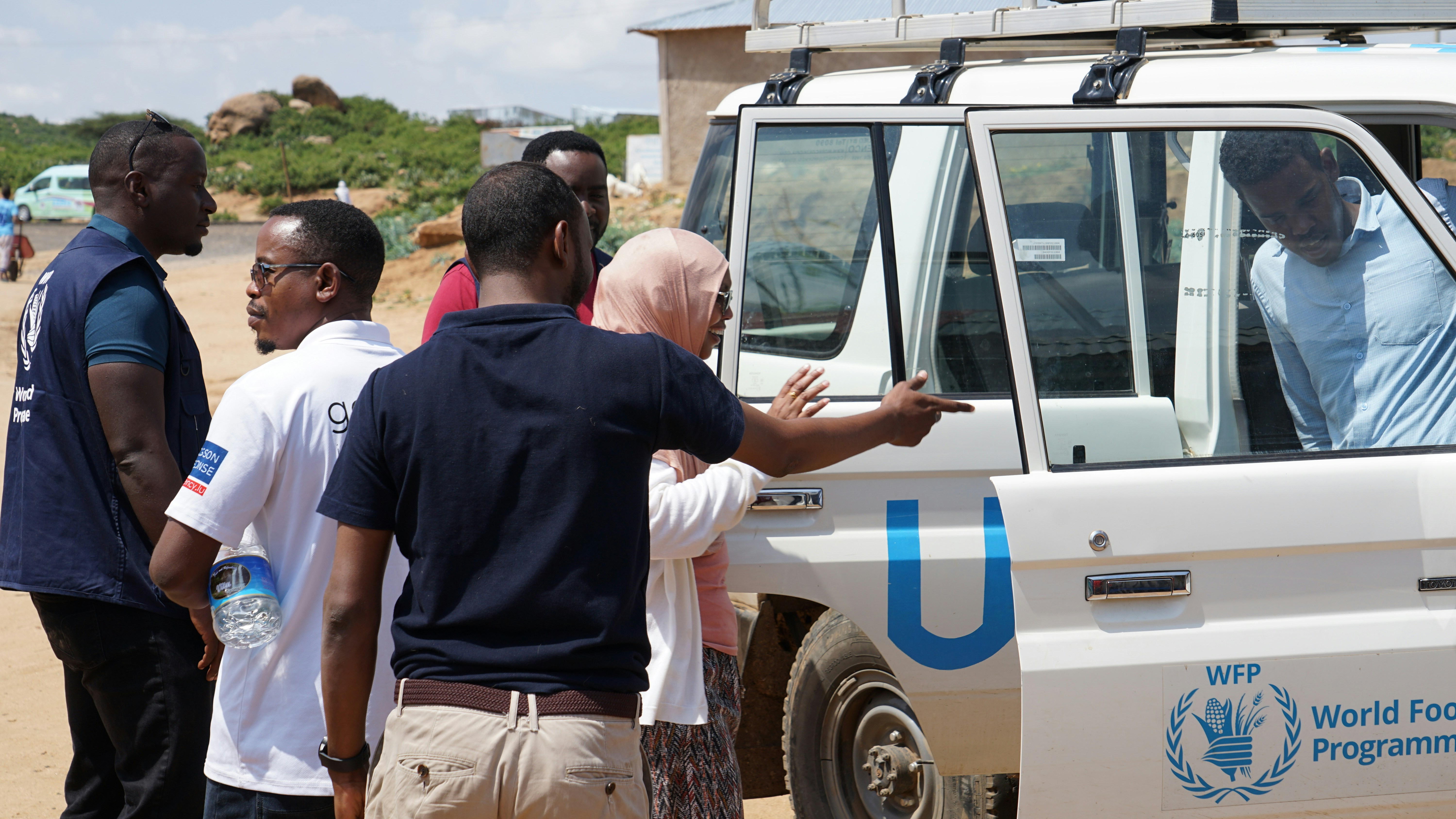 People stand near a white world food programme vehicle.
