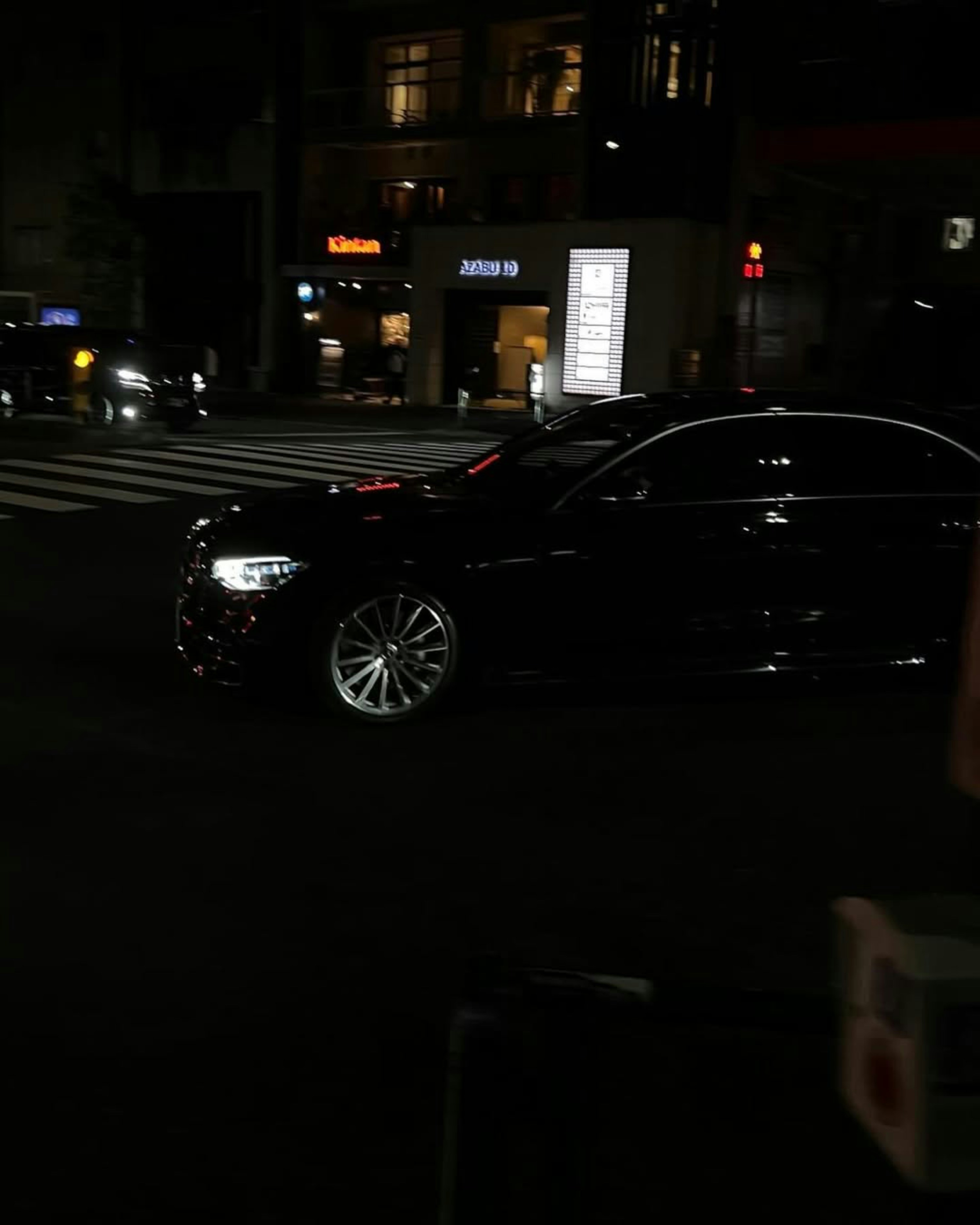A dark sedan drives through a city street at night.