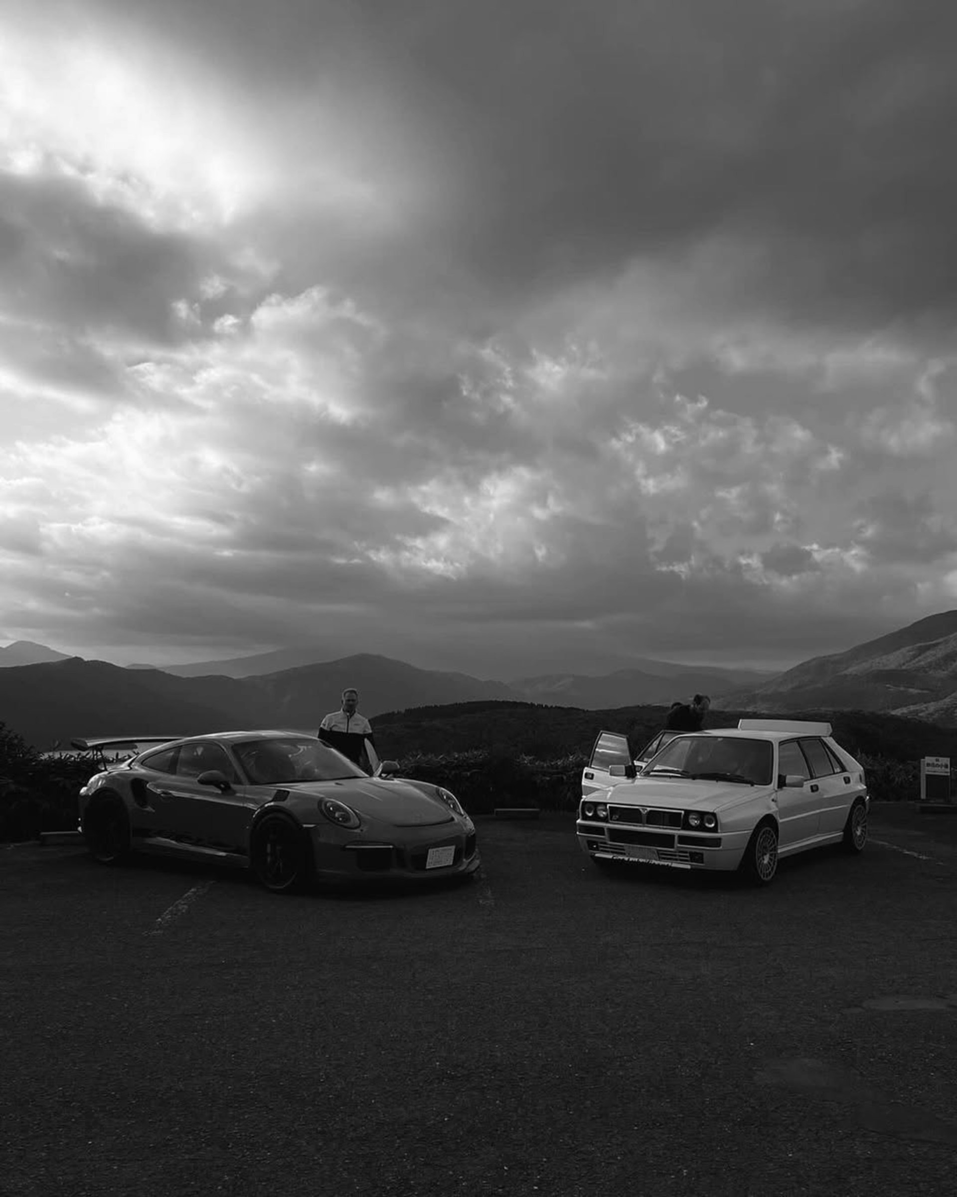 Two cars park against a dramatic mountain backdrop.
