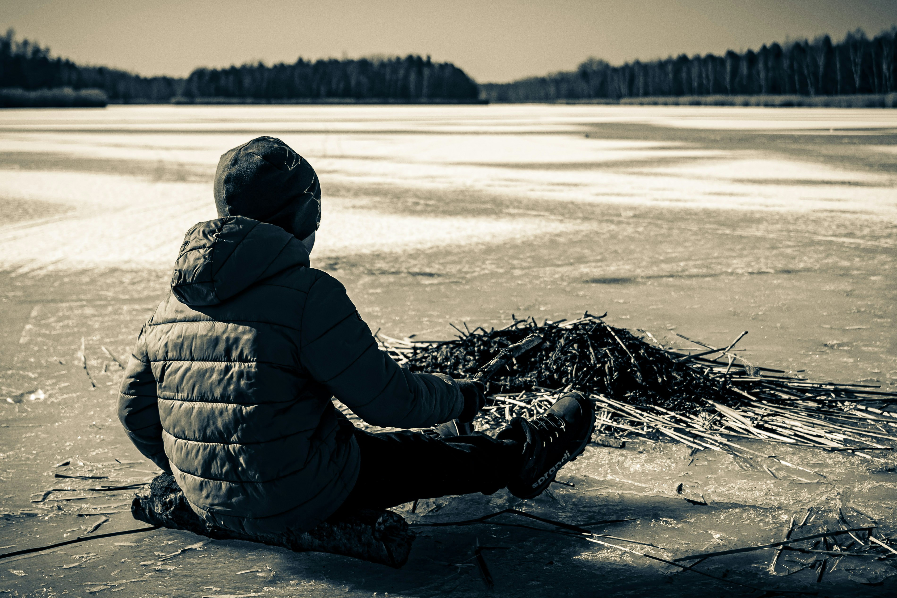 A child sits on ice, gazing at the lake.