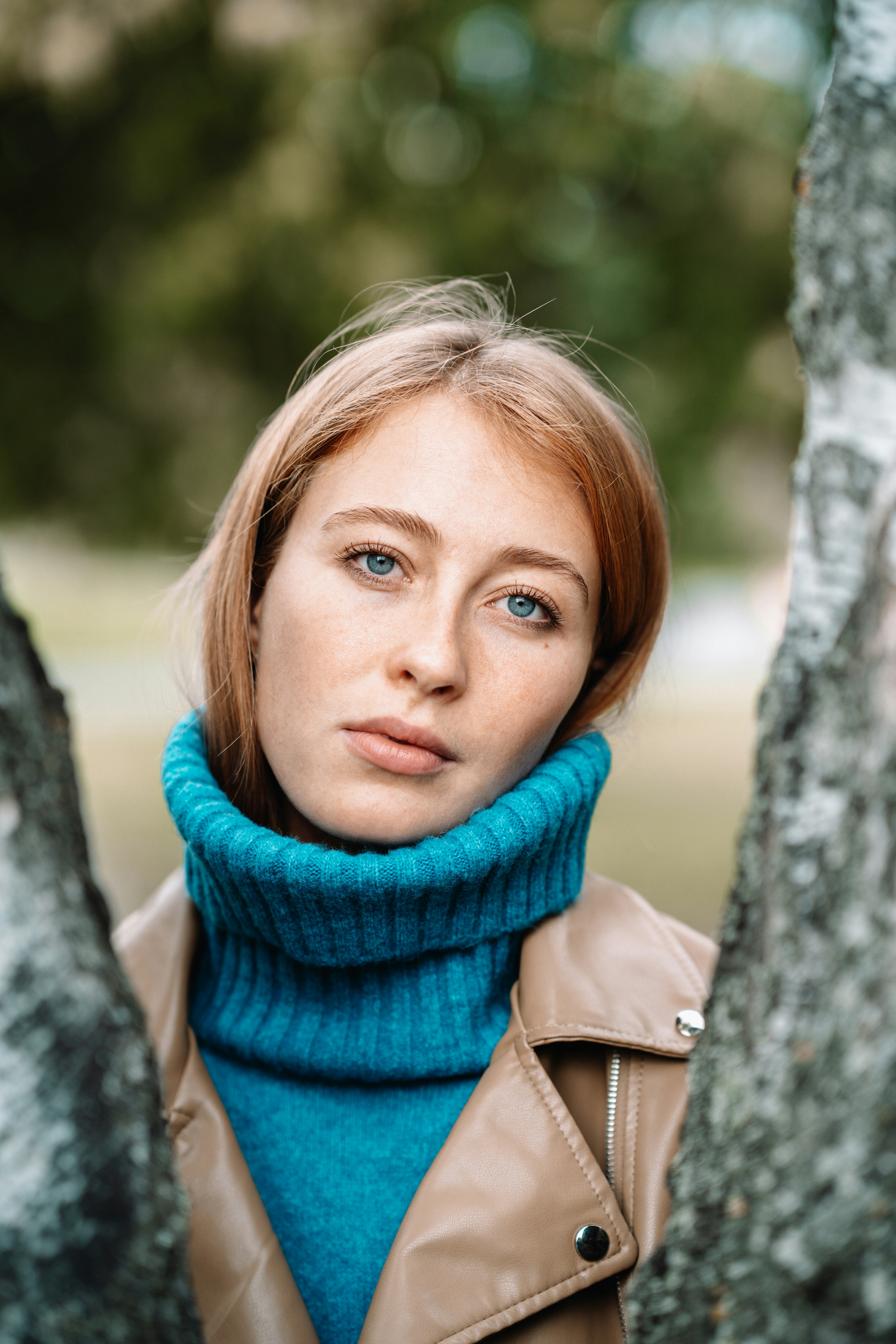 A woman with red hair looks between trees.