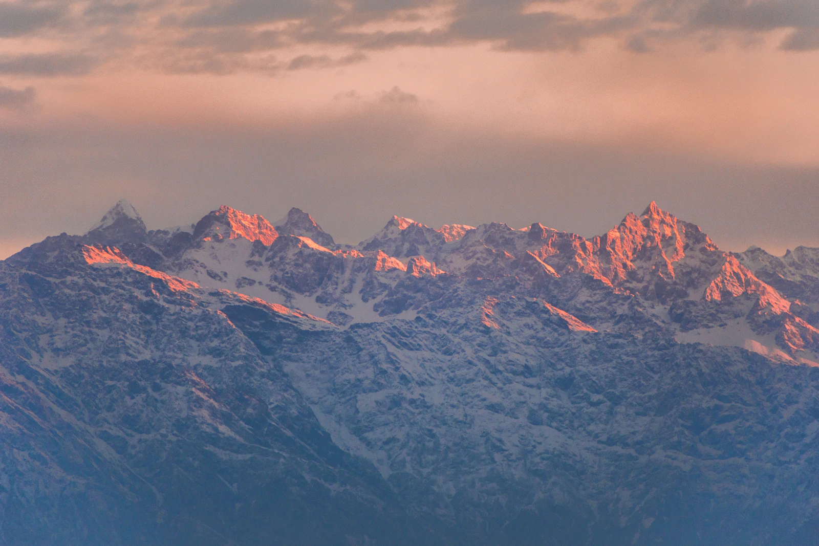 Himalayan peaks north of Kathmandu catching pink light above blue haze, seen from Bhasmasur hill on the valley's southern rim