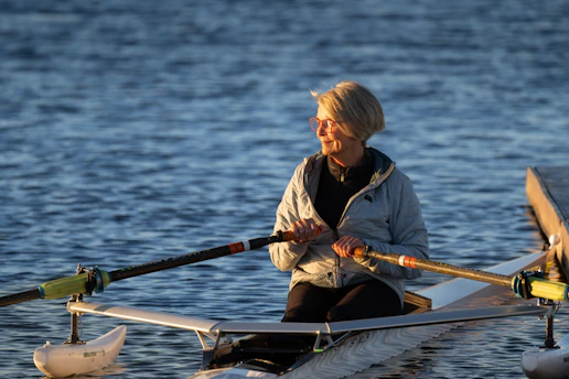 A woman rows her boat on calm water.